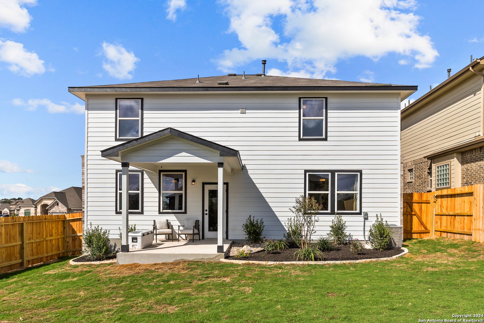 Rear view of two-story white Davidson Homes Douglas F with covered patio, large windows, and fenced backyard in Bricewood, San Antonio
