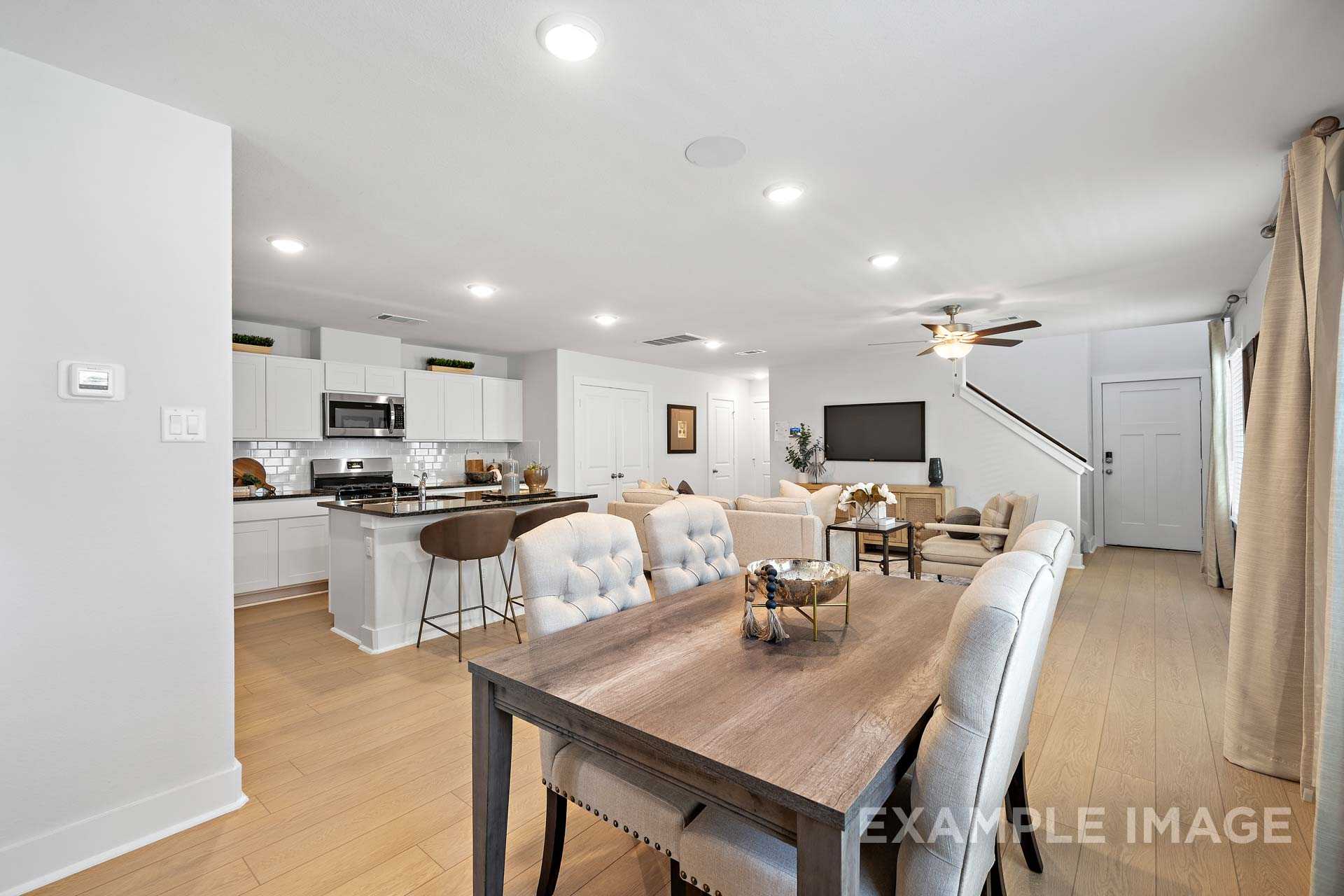 Open-concept kitchen and living area in The Rose B with white cabinetry, large island, dining table, and cozy seating