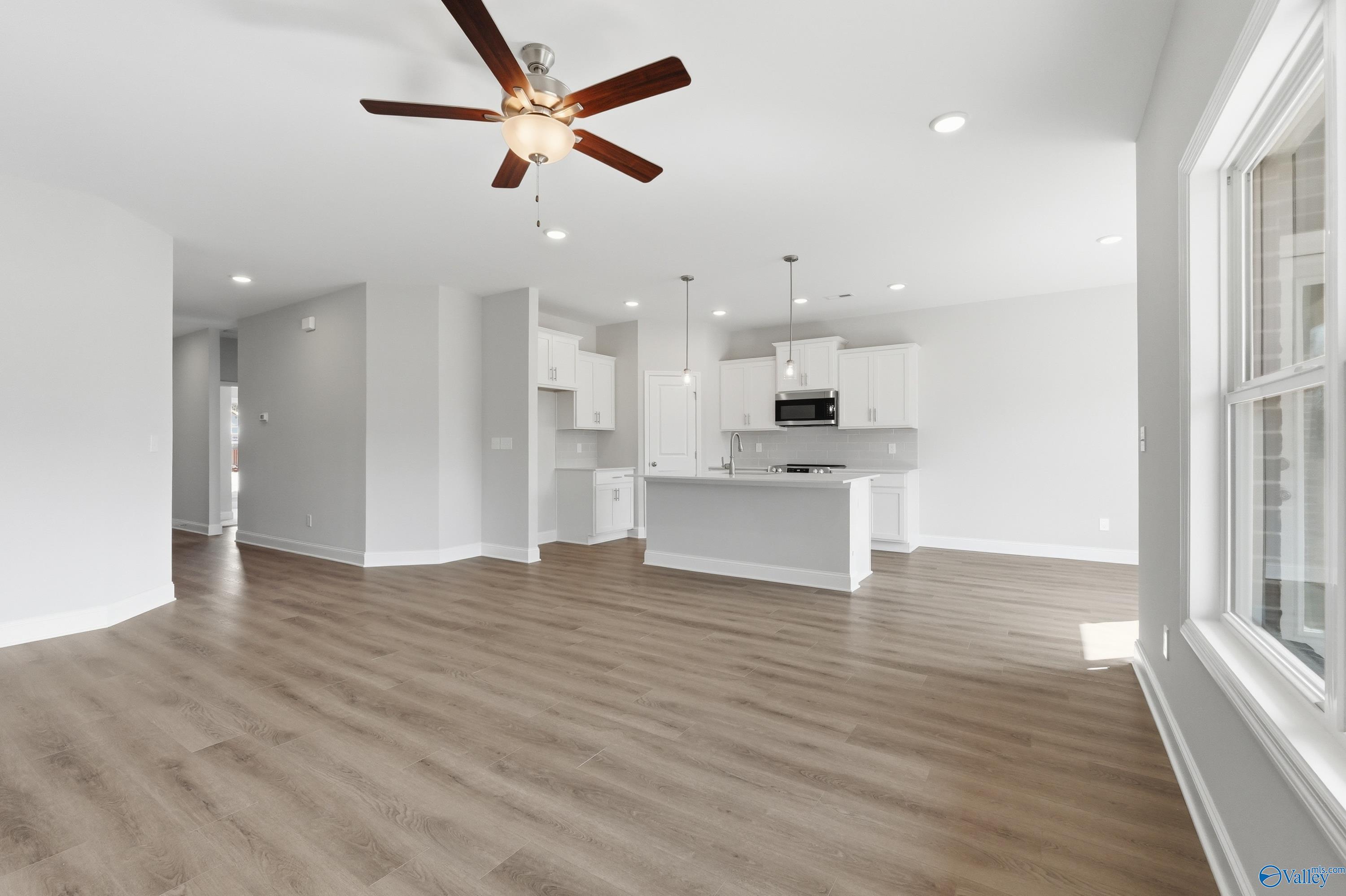Bright open-concept kitchen-living area with white cabinets, island, ceiling fan, and hardwood floors in Davidson Homes The Asheville C, Huntsville, AL