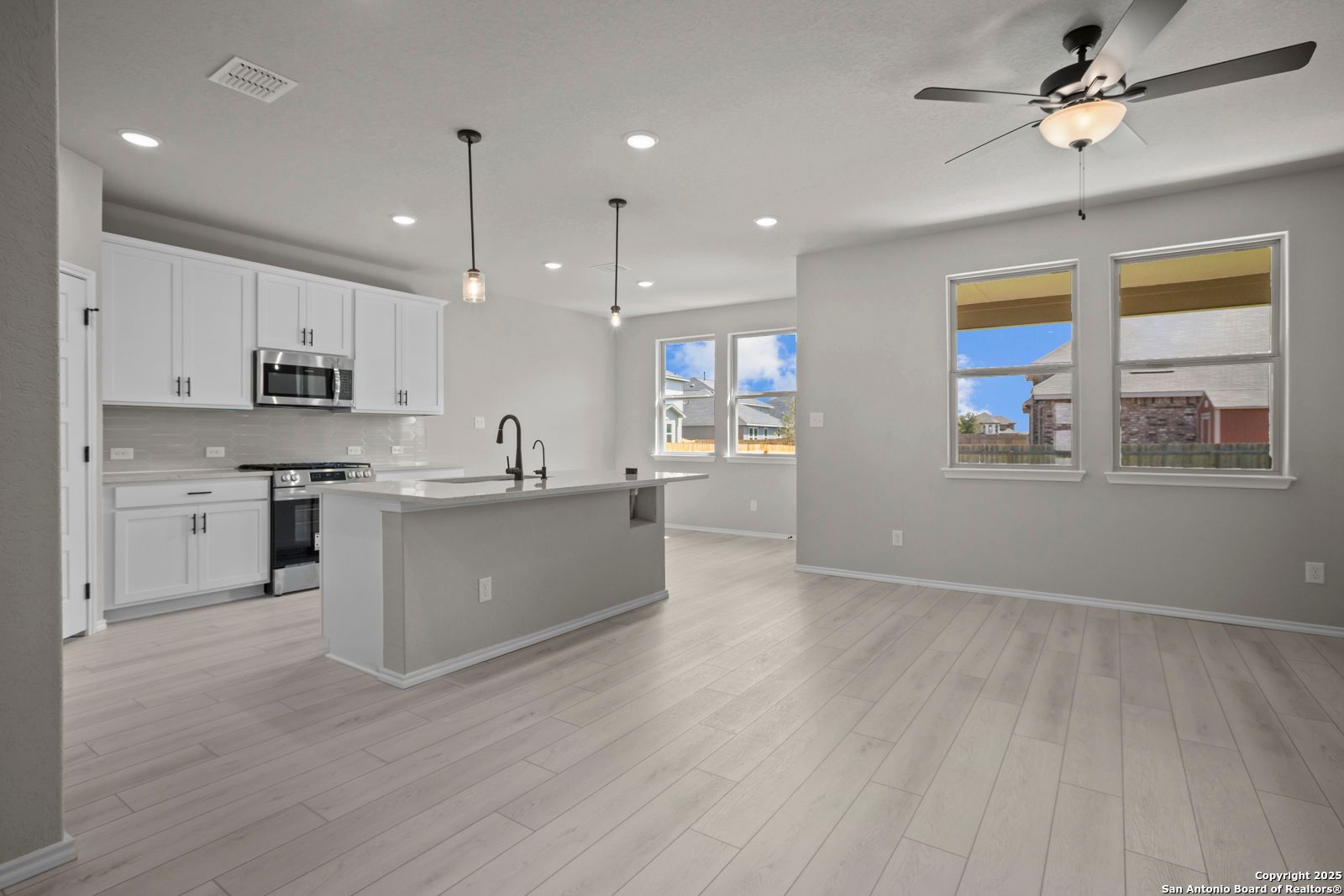 Modern open kitchen featuring white cabinets, stainless appliances, large island, and pendant lights in Davidson Homes The Asheville E, Converse, Texas