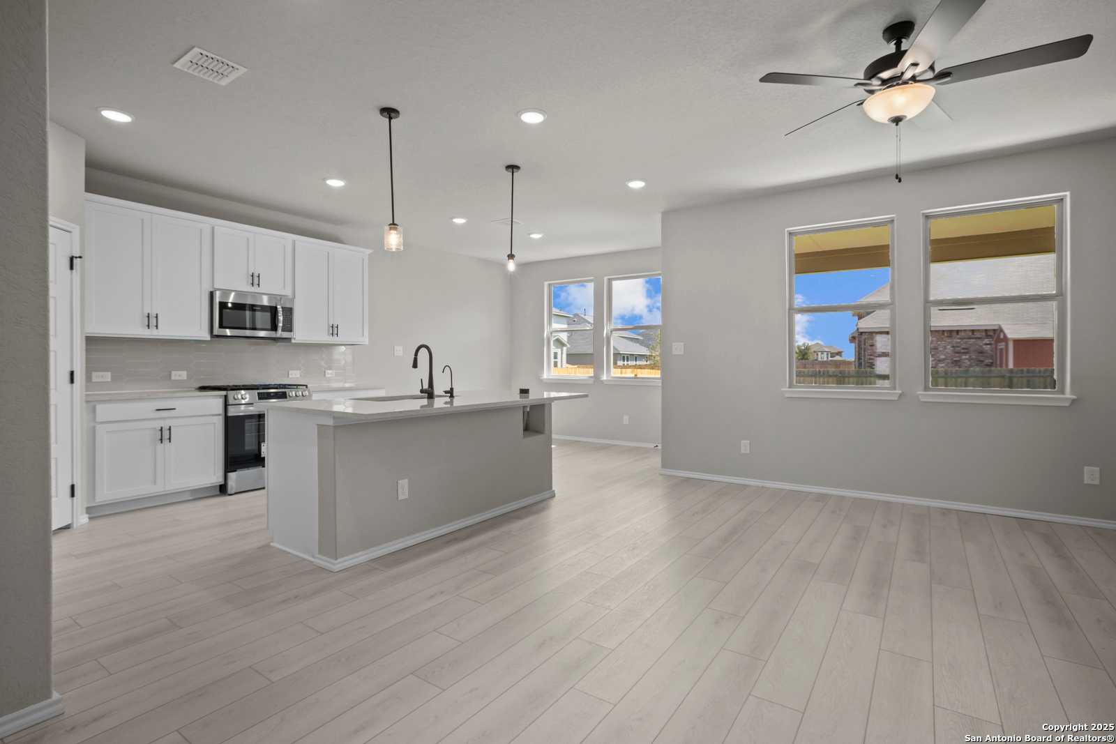 Modern open kitchen featuring white cabinets, stainless appliances, large island, and pendant lights in Davidson Homes The Asheville E, Converse, Texas
