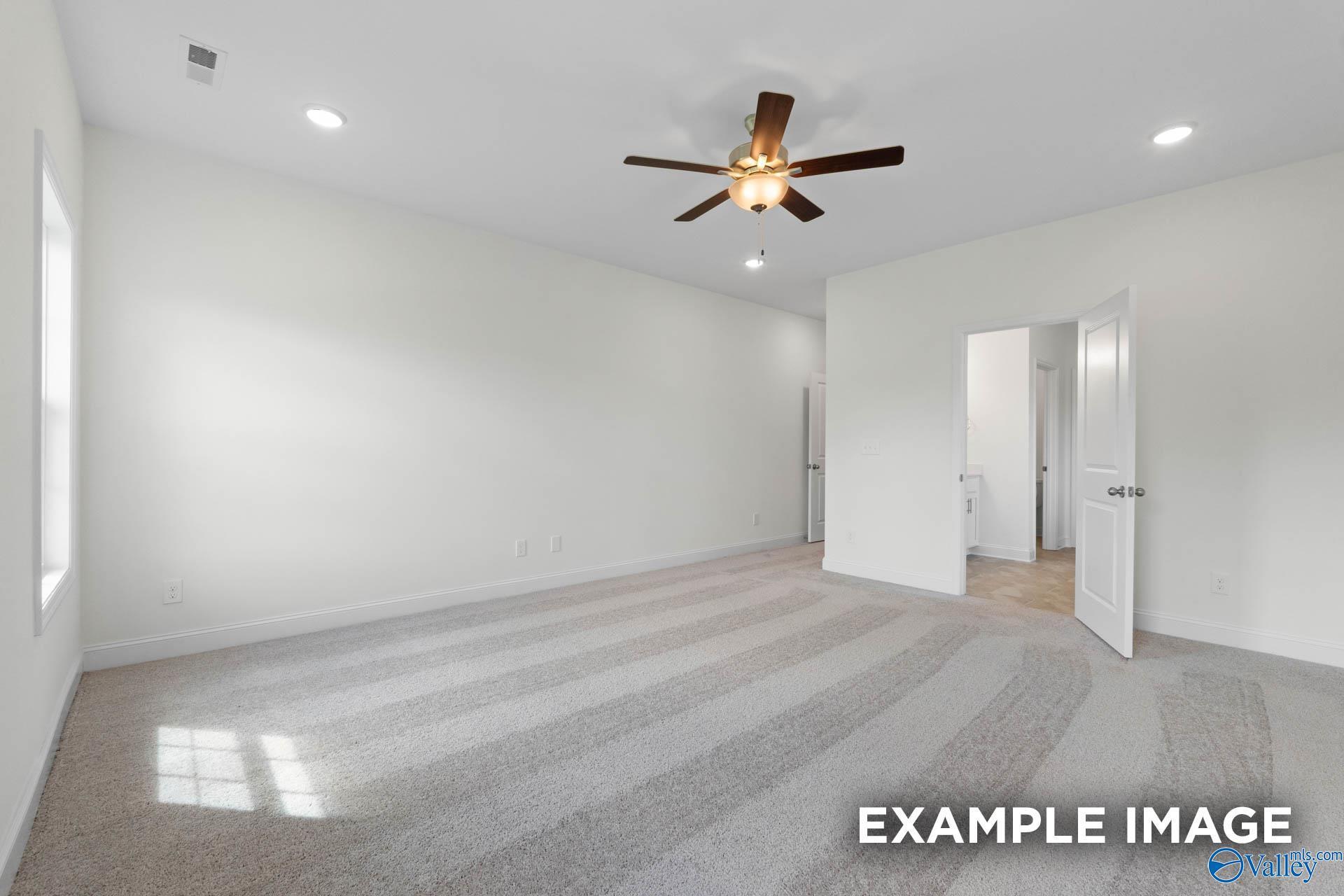 Bright living room with white walls, ceiling fan, beige carpet, and adjacent rooms in Davidson Homes Rockford B, Athens Alabama