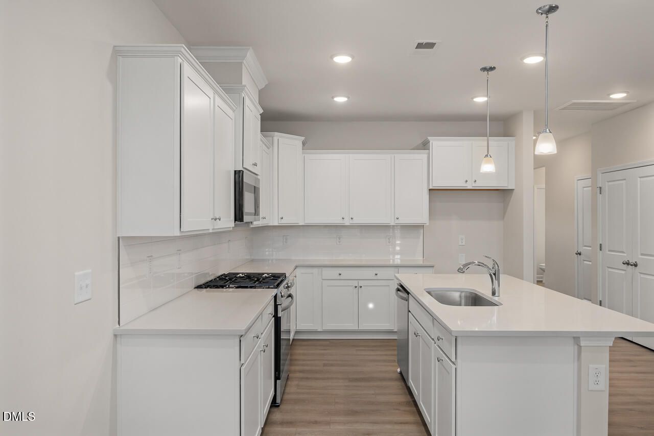 Modern white shaker kitchen with large island, stainless appliances, subway tile backsplash in The Graham plan by Davidson Homes, Fuquay-Varina, NC