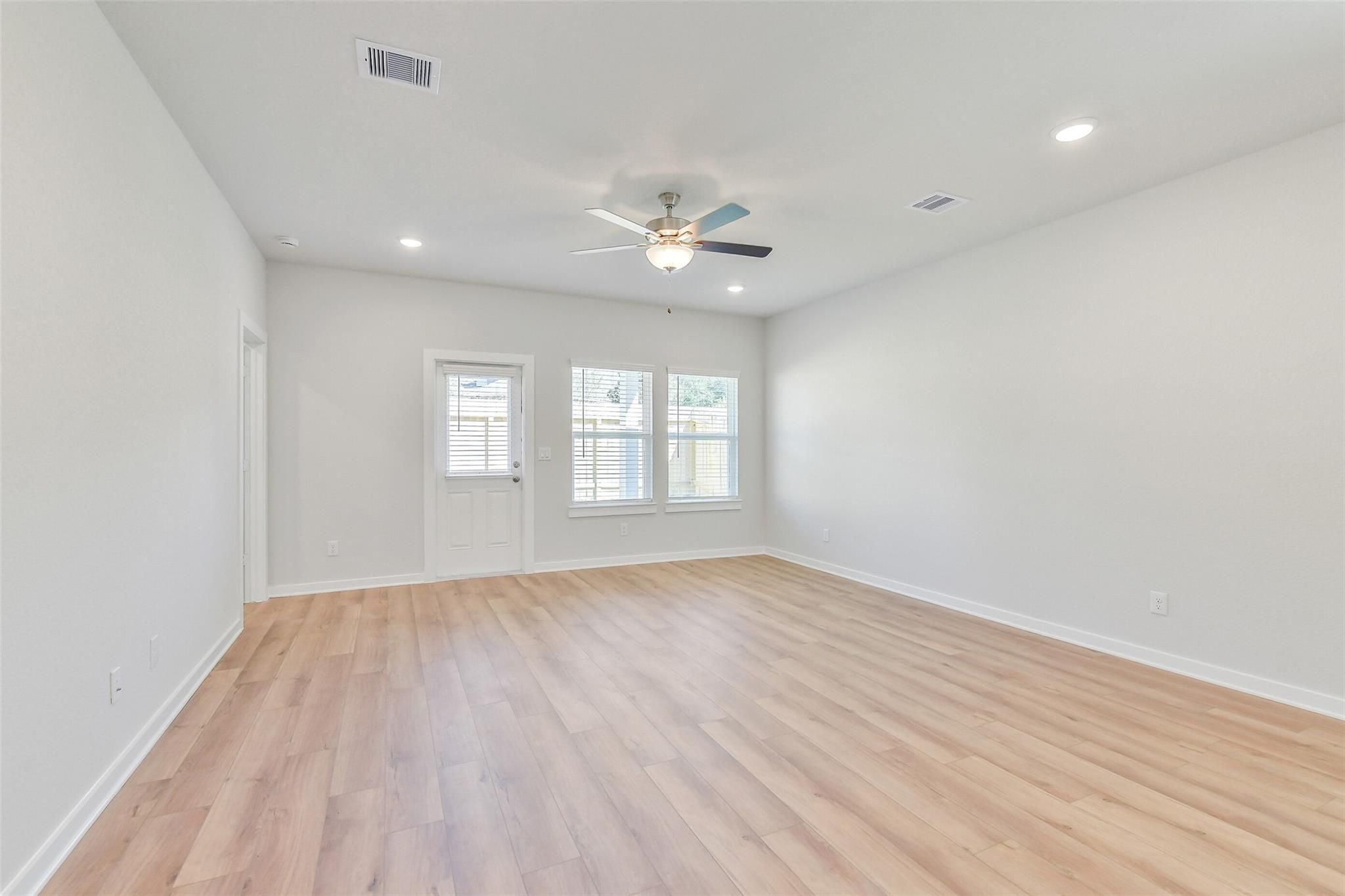Bright living room with light gray walls, oak hardwood floors, ceiling fan, and large windows in Davidson Homes Blanco E, Magnolia, Texas