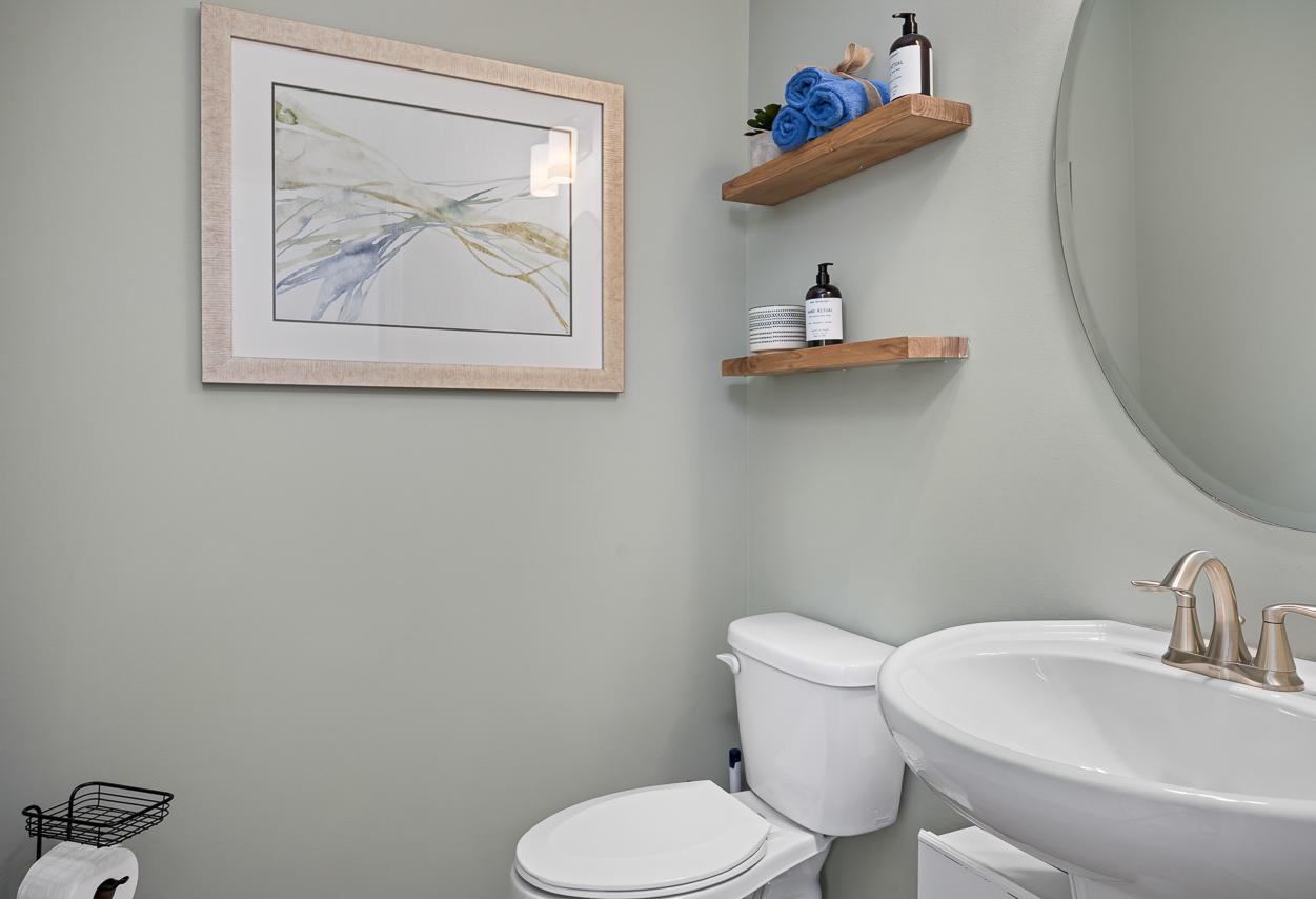 Modern powder room in The Wake by Davidson Homes featuring a pedestal sink, floating wood shelves, and elegant wall art.