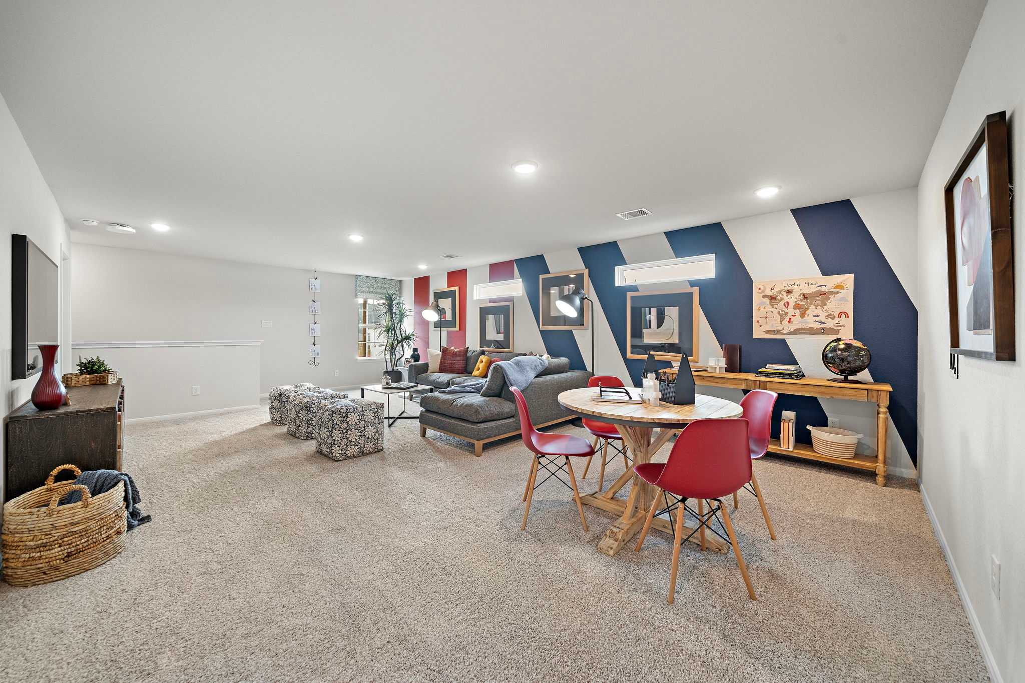 Spacious bonus room at Liberty Estates in Cleveland Texas with striped accent wall, gray sectional sofa, red chairs, and round table
