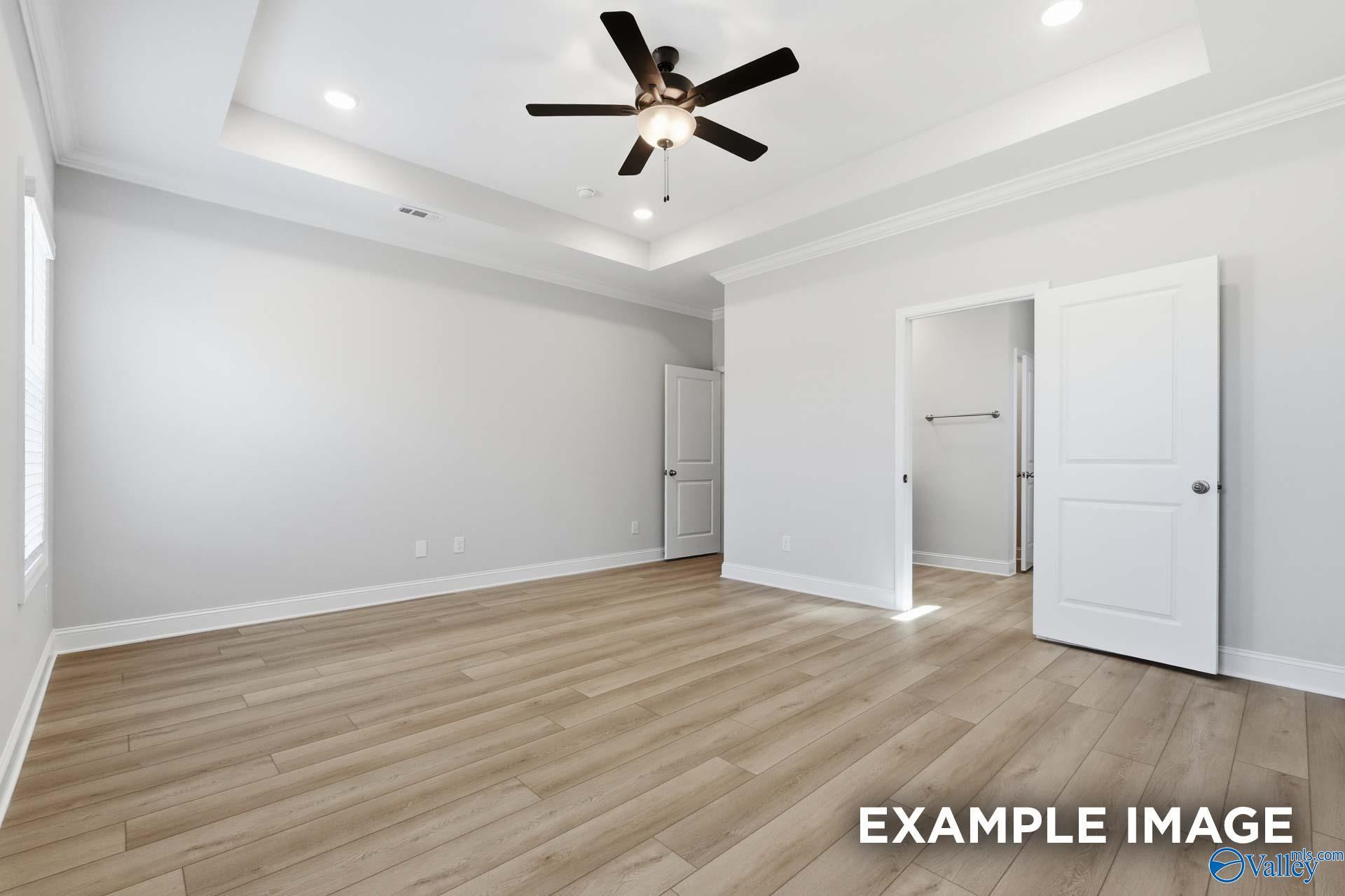 Spacious master bedroom with tray ceiling, ceiling fan, light oak floors, and walk-in closet in Davidson Homes The Harrison C, Madison, Alabama