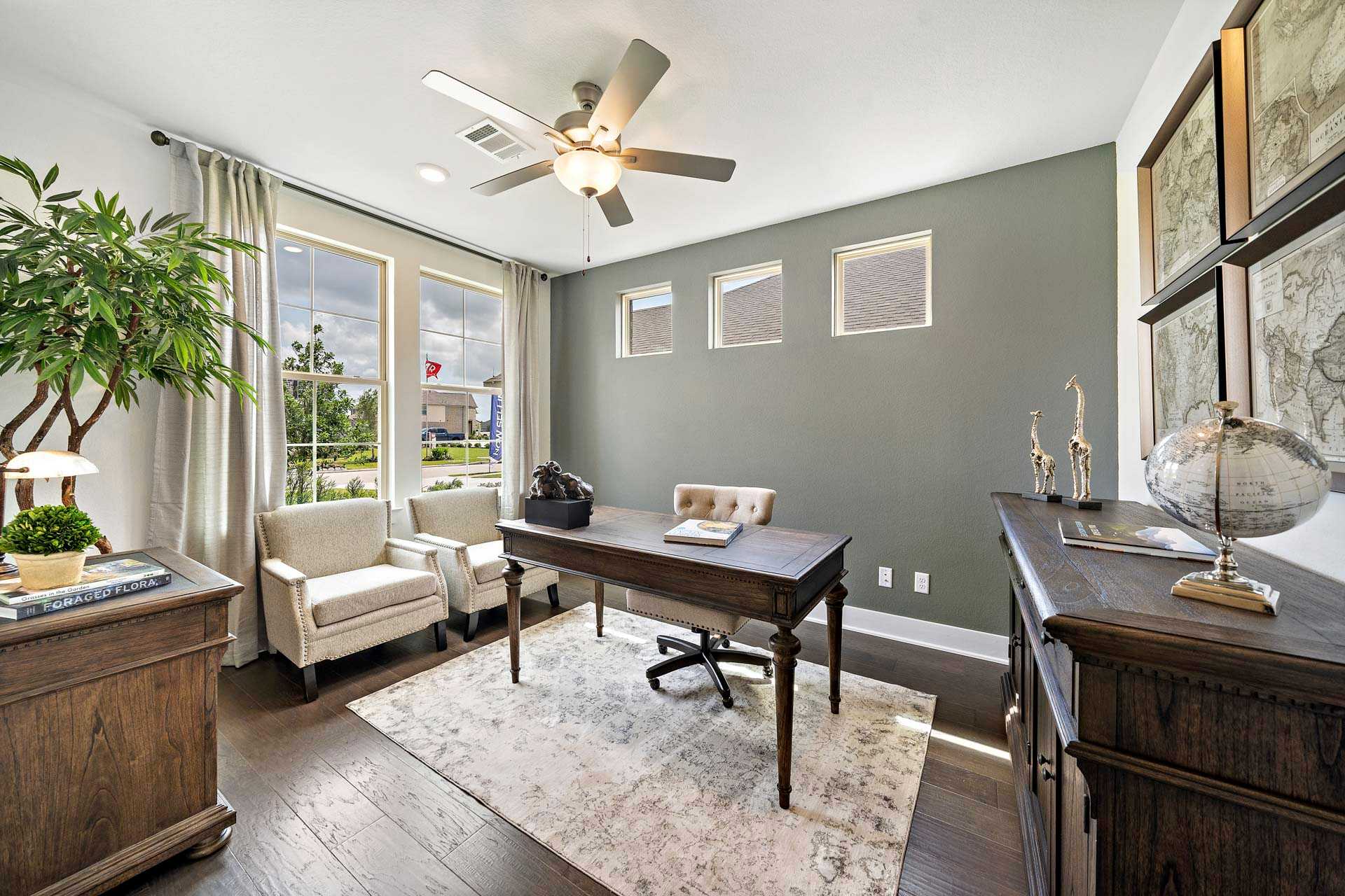 Cozy home office in Sierra Vista Rosharon Texas by Davidson Homes with wooden desk, armchairs, ceiling fans, and potted plants