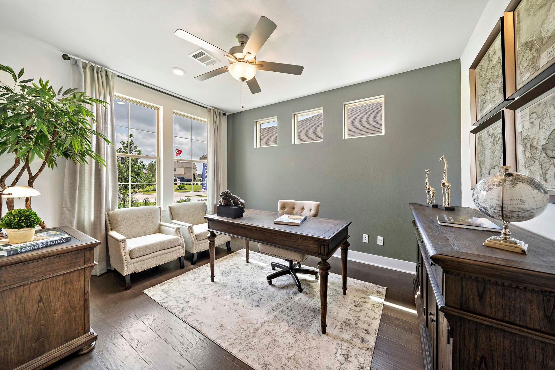 Cozy home office in Sierra Vista Rosharon Texas by Davidson Homes with wooden desk, armchairs, ceiling fans, and potted plants