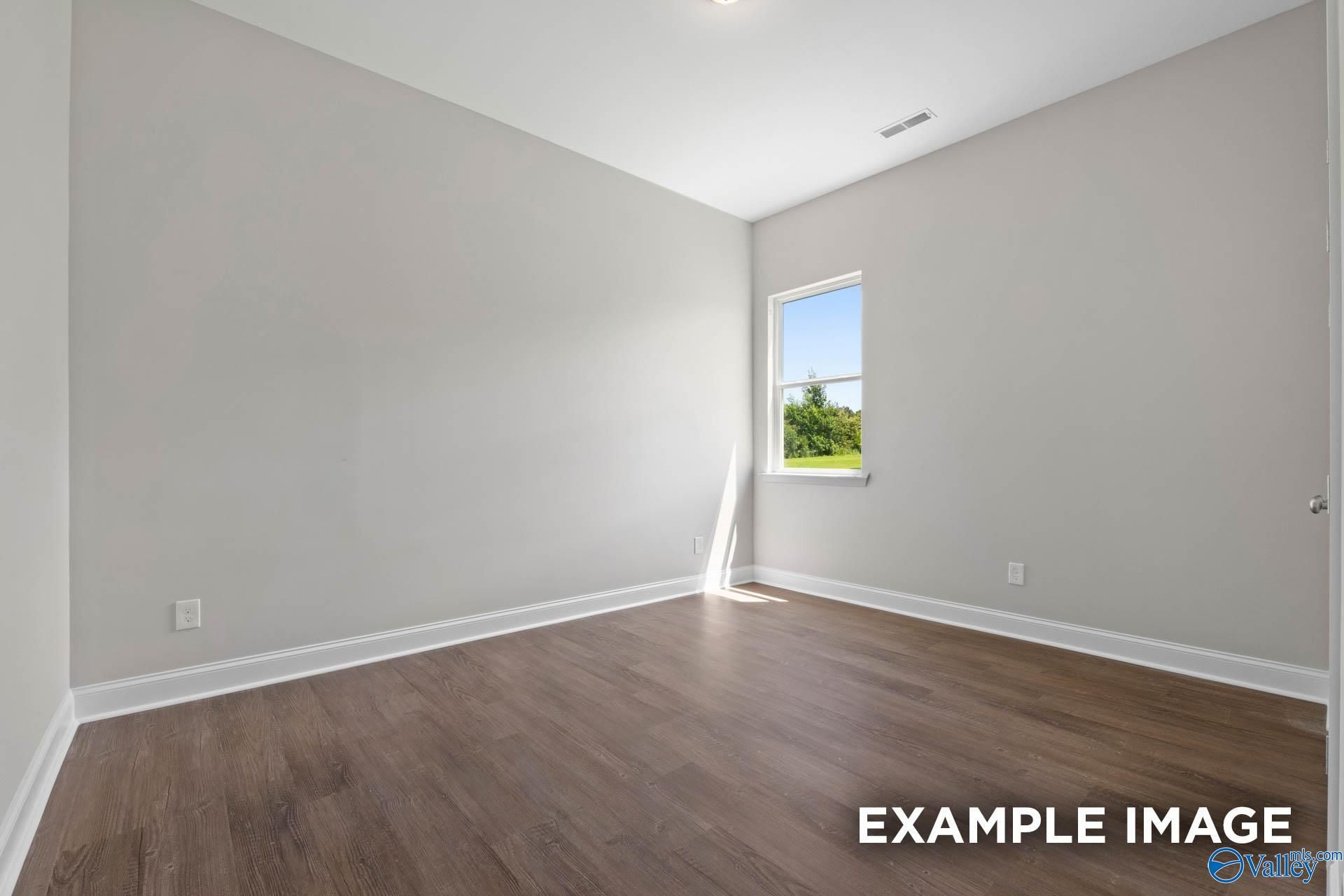 Bright secondary bedroom with light gray walls, hardwood floors, and window overlooking trees in Evermore Homes The Arcadia, Owens Cross Roads, Alabama