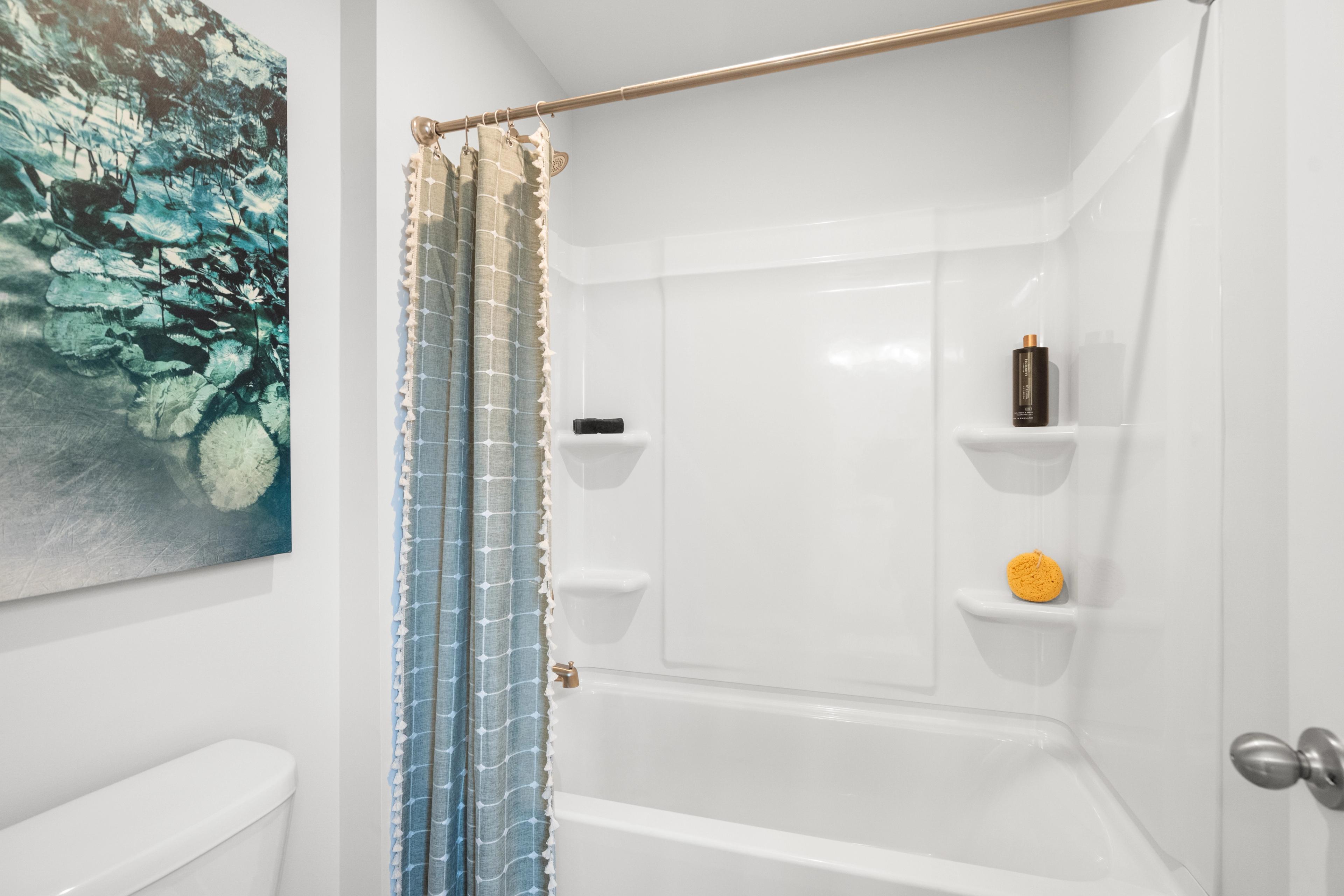 Contemporary bathroom at Stegall Village in Emerson GA by Davidson Homes featuring white bathtub, ombre shower curtain, and abstract wall art