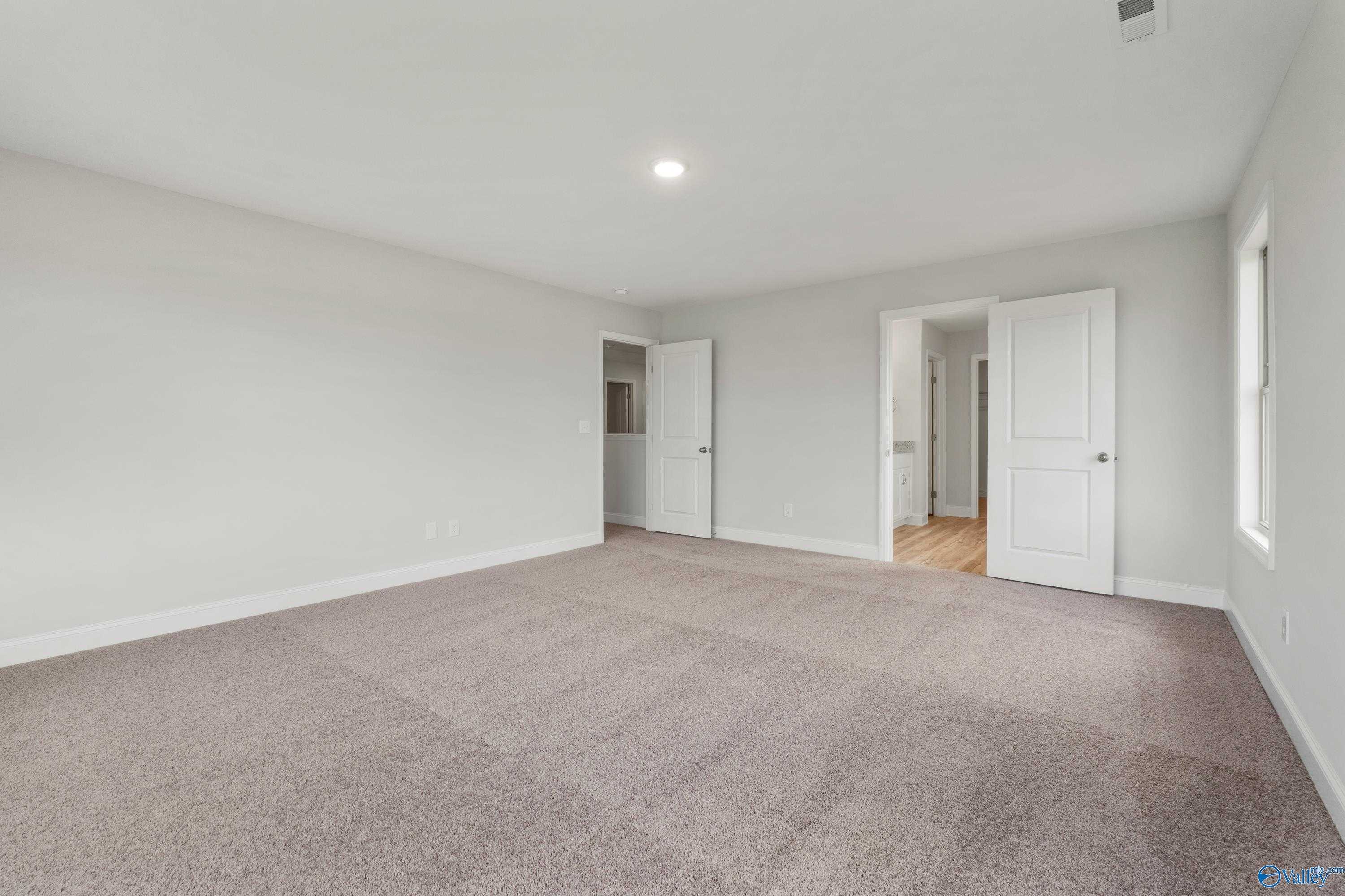 Spacious empty bedroom with neutral walls, beige carpet, en-suite bath door in 4-bed Davidson Homes Chelsea C, Harvest Alabama