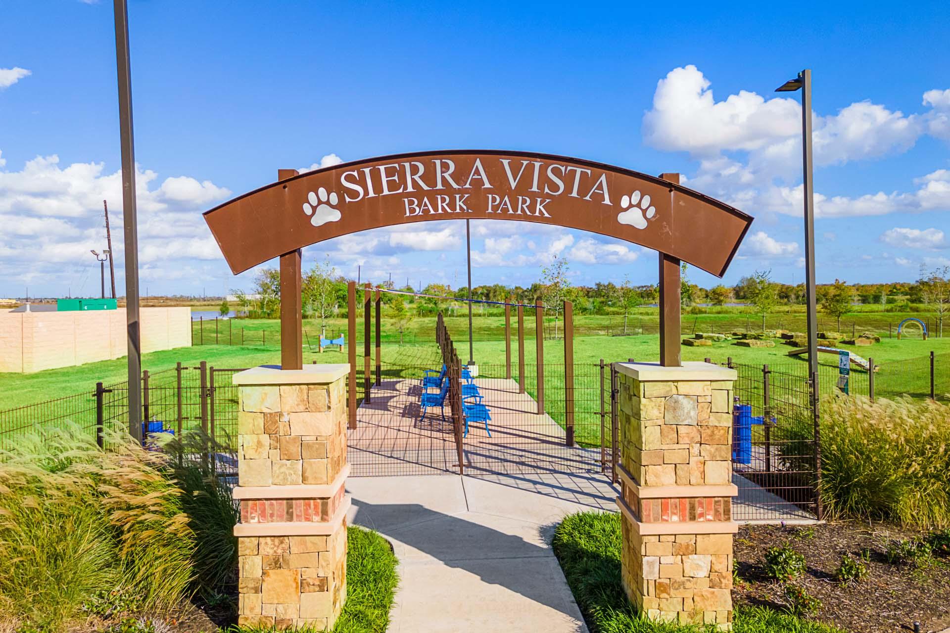 Sierra Vista Bark Park entrance arch with paw prints, stone pillars, blue benches, and fenced grassy area in Rosharon Texas