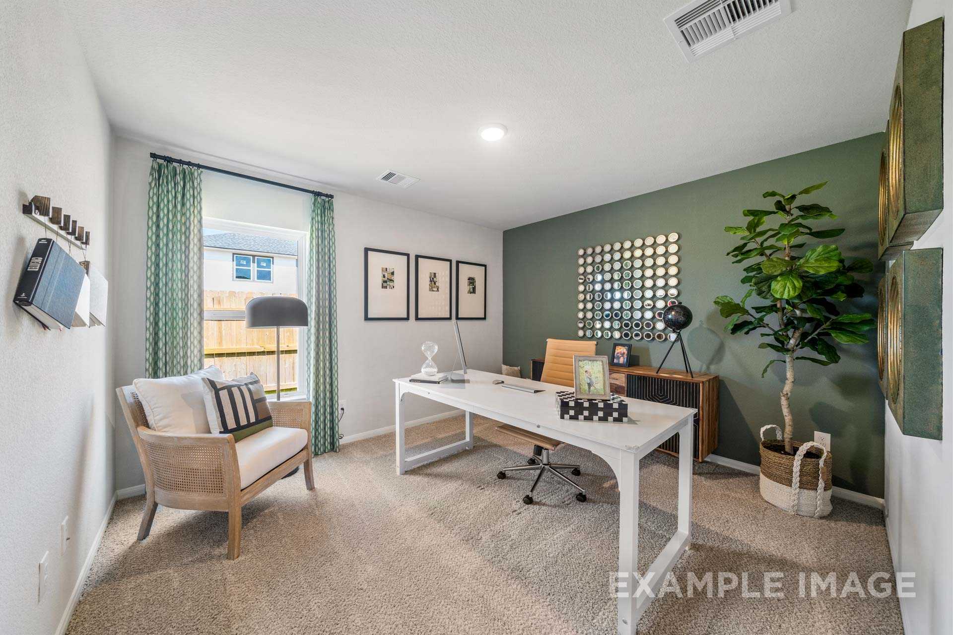 Spacious home office in The Acadia B model with white desk, green accent wall, potted plants, and large window overlooking yard