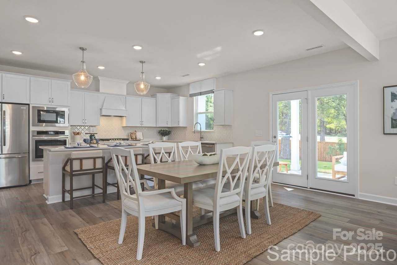 Spacious dining area with wooden table, white chairs, and open white kitchen in Davidson Homes The Hickory E II, Enclave at Belmont, NC