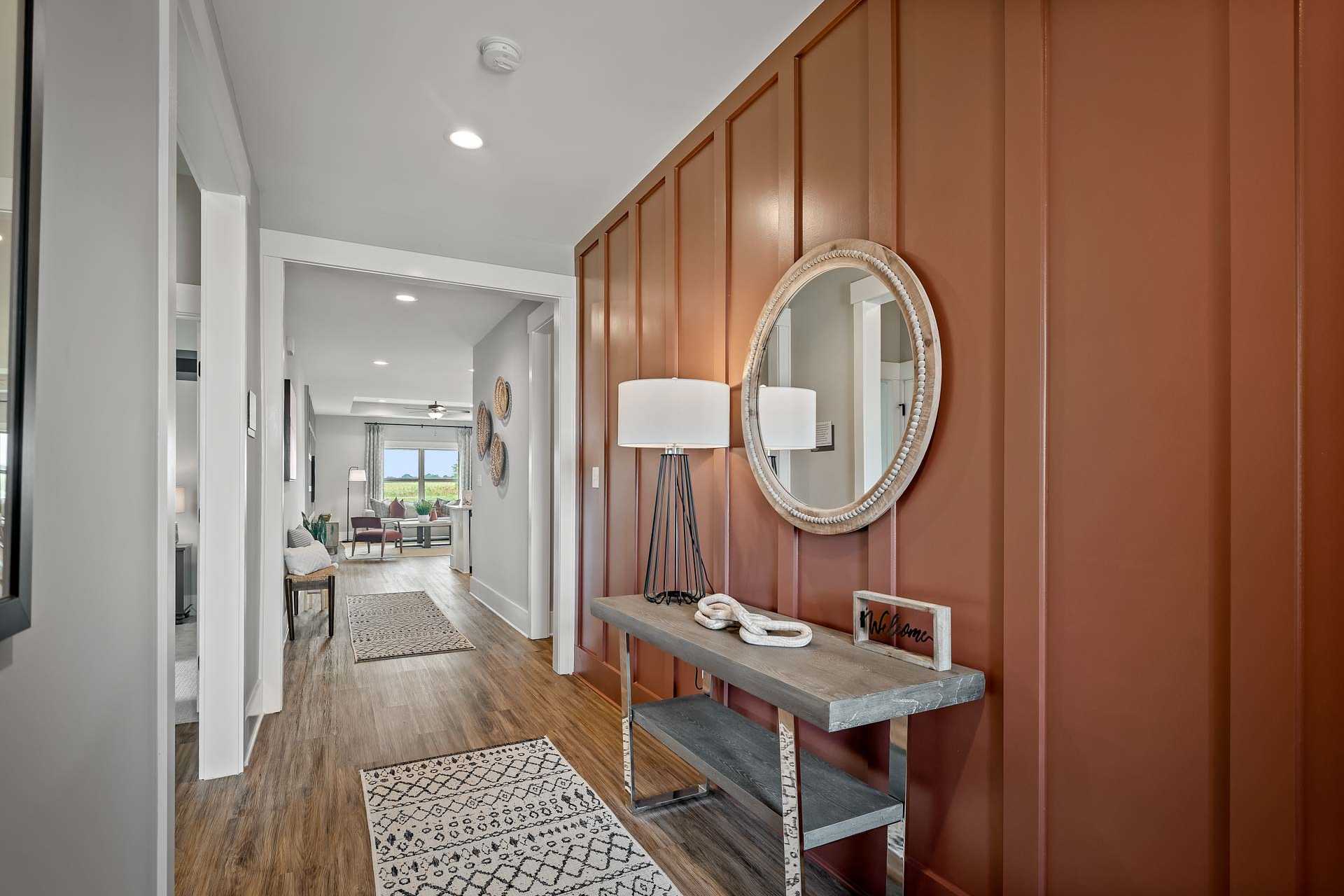 Modern entryway hallway at Heritage Lakes in New Market AL with rust accent wall, round mirror, console table, and hardwood floors