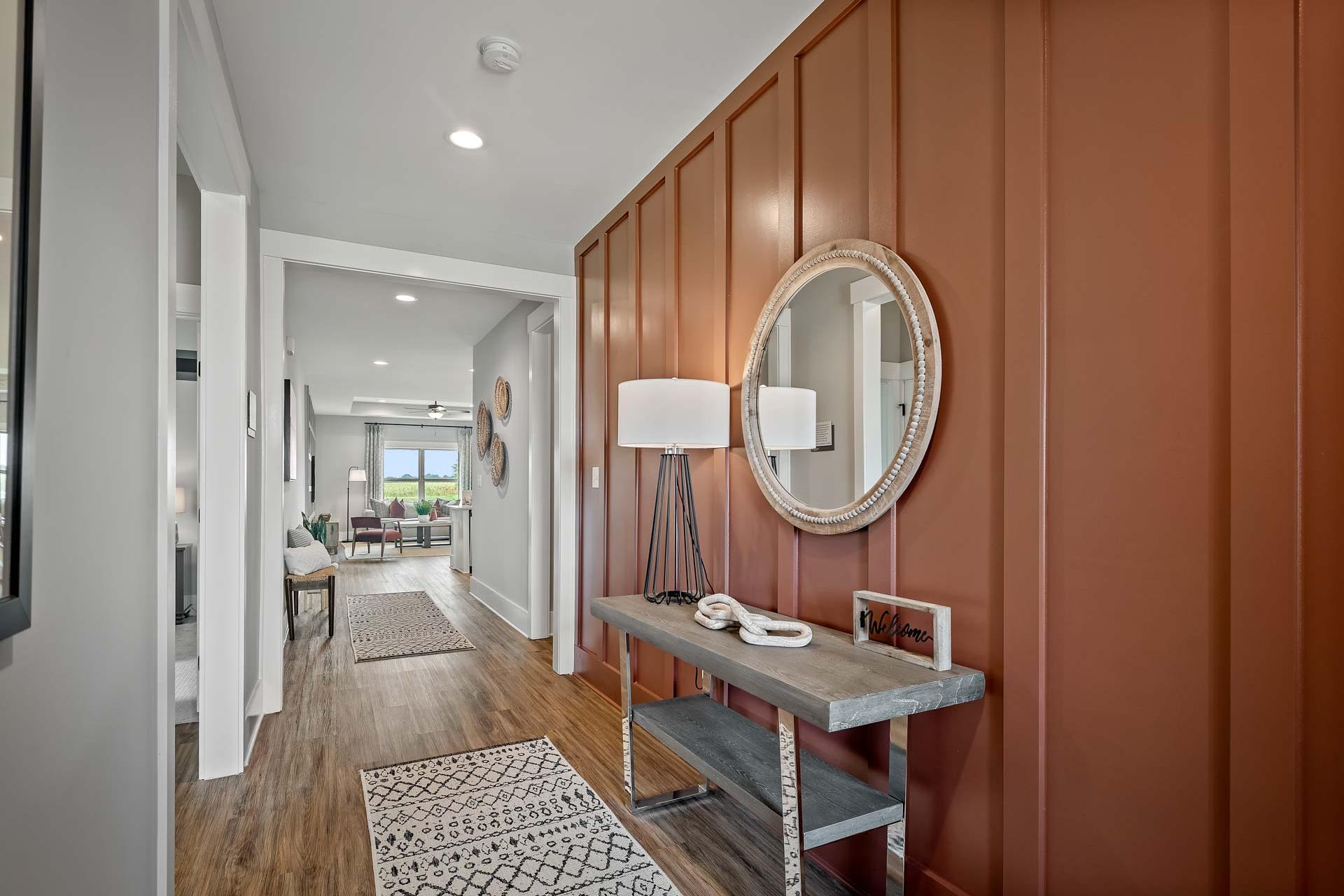 Modern entryway hallway at Heritage Lakes in New Market AL with rust accent wall, round mirror, console table, and hardwood floors