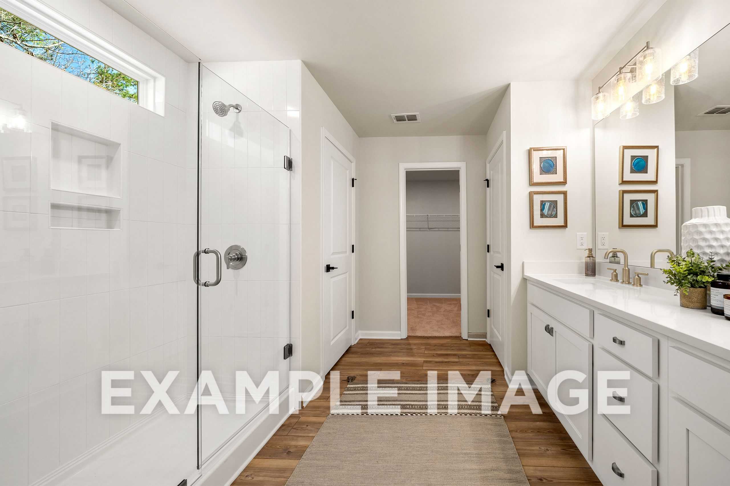 Spacious master bathroom in The Hickory A with glass walk-in shower, double white vanity, and closet doorway