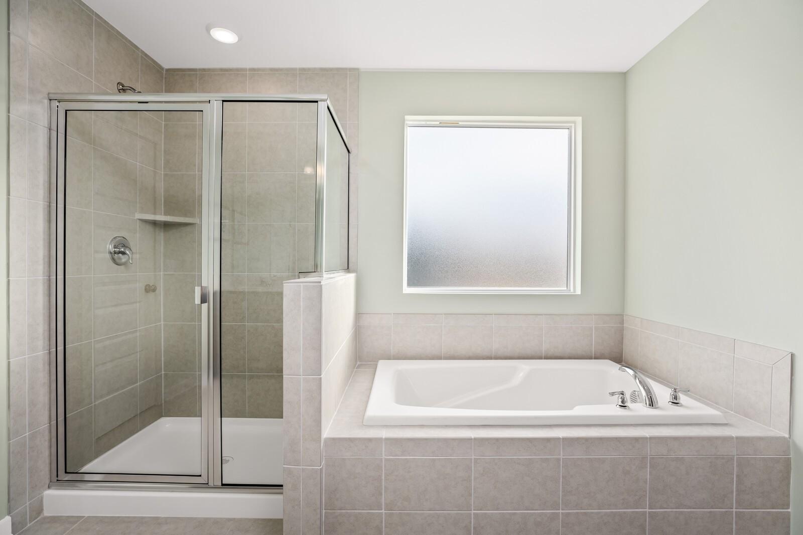 Elegant master bathroom featuring glass-enclosed shower, white soaking tub, and frosted window in Davidson Homes The Gordon C, White House, TN