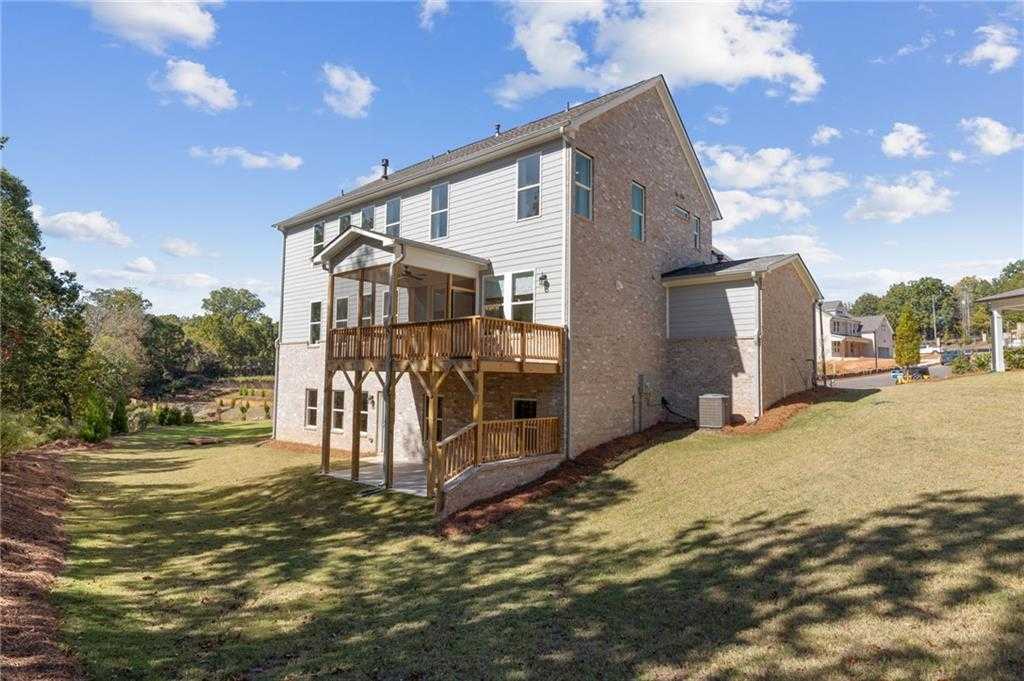 Two-story Danbury C home exterior with upper wooden deck and three-car garage in lush green yard, Melody Lakeside Estates, Buford, Georgia