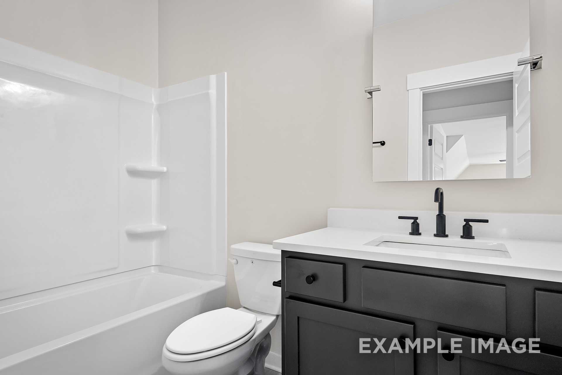 Modern master bathroom in The Hawkins by Davidson Homes featuring white tub, glass shower, dark vanity, and black faucet