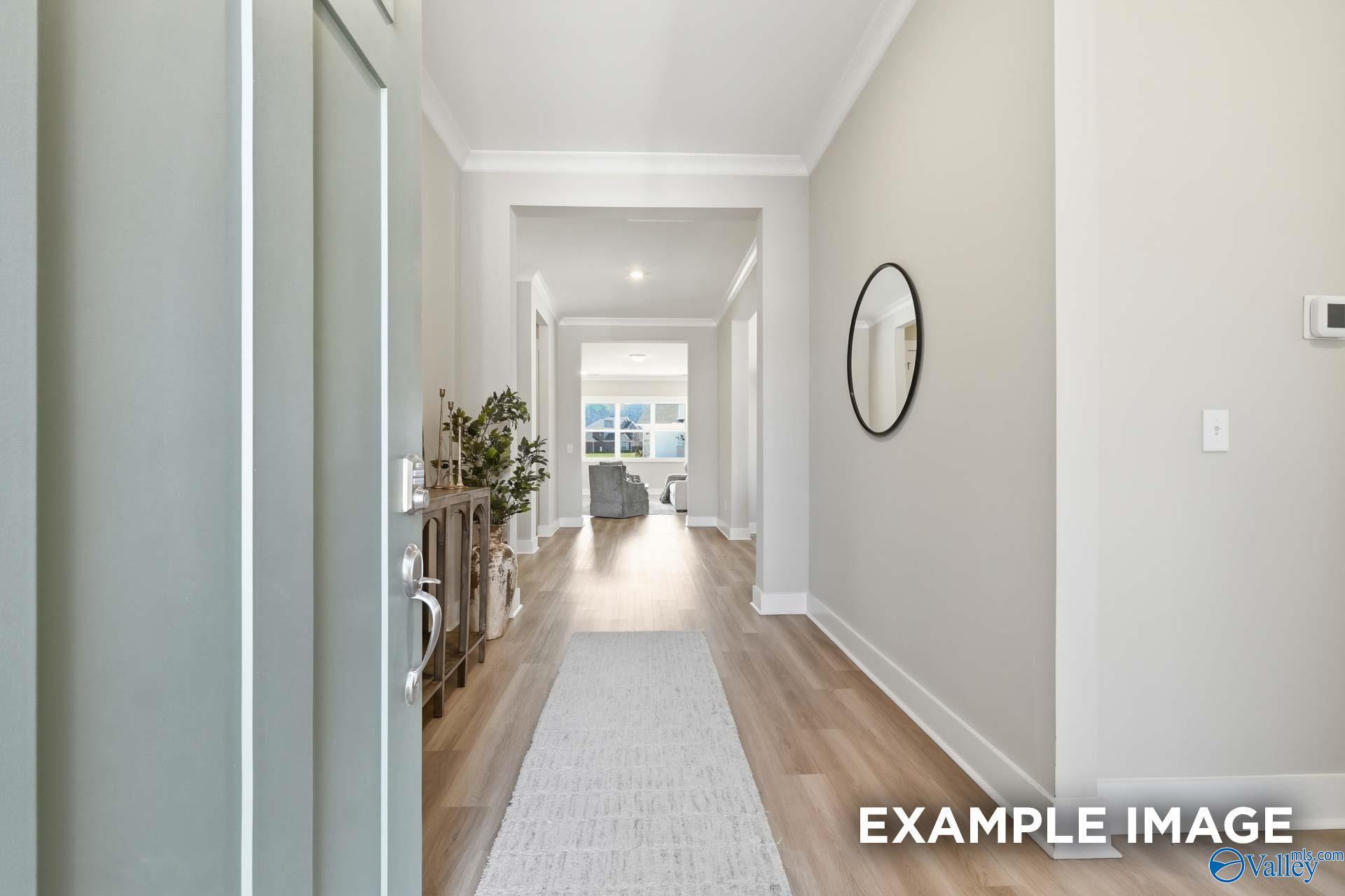 Welcoming entry hallway with hardwood floors, beige walls, runner rug, console table, and round mirror in 5-bedroom Evermore Homes The Oxford B, Owens Cross Roads, Alabama