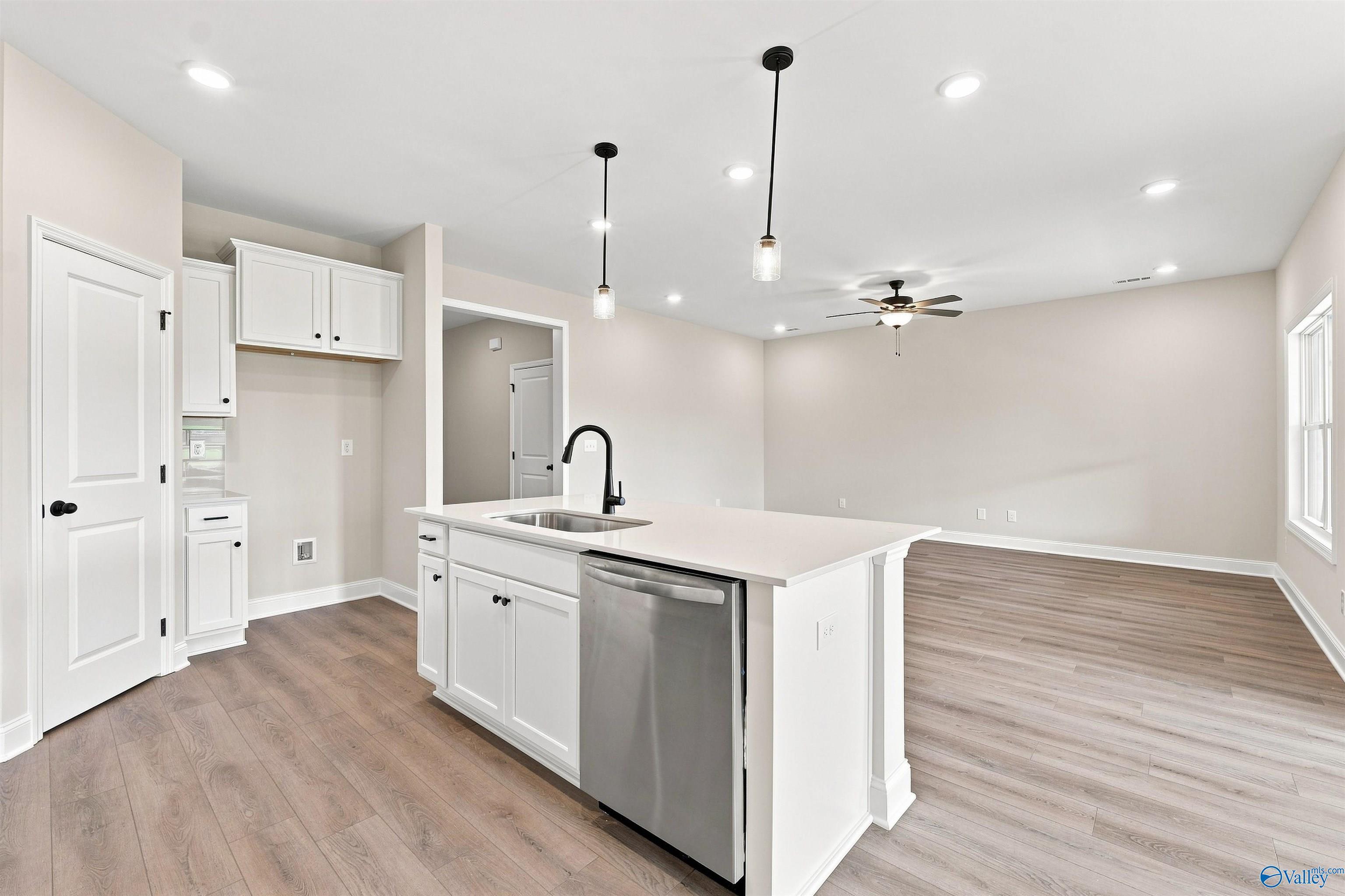White kitchen island with sink and pendant lights flowing into open living area in Davidson Homes The Everett B, Toney, Alabama