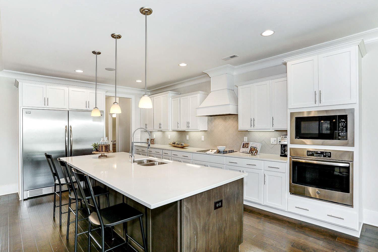 Spacious modern kitchen in The Finleigh featuring white shaker cabinets, quartz island with bar stools, stainless steel appliances, and pendant lights