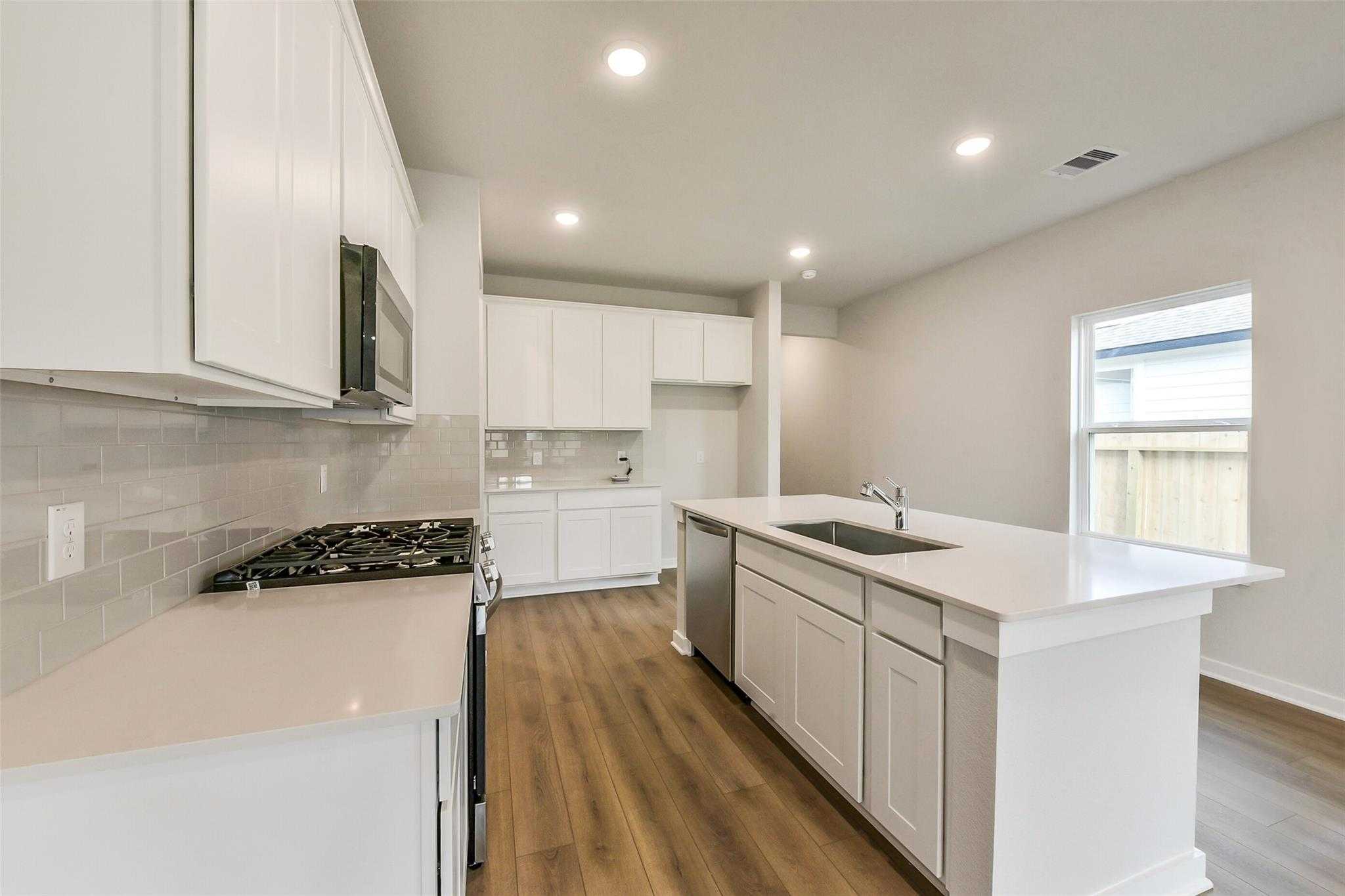 Modern white kitchen with large island sink, gas range, stainless appliances, and subway tile in The Frio G by Davidson Homes, Dayton TX