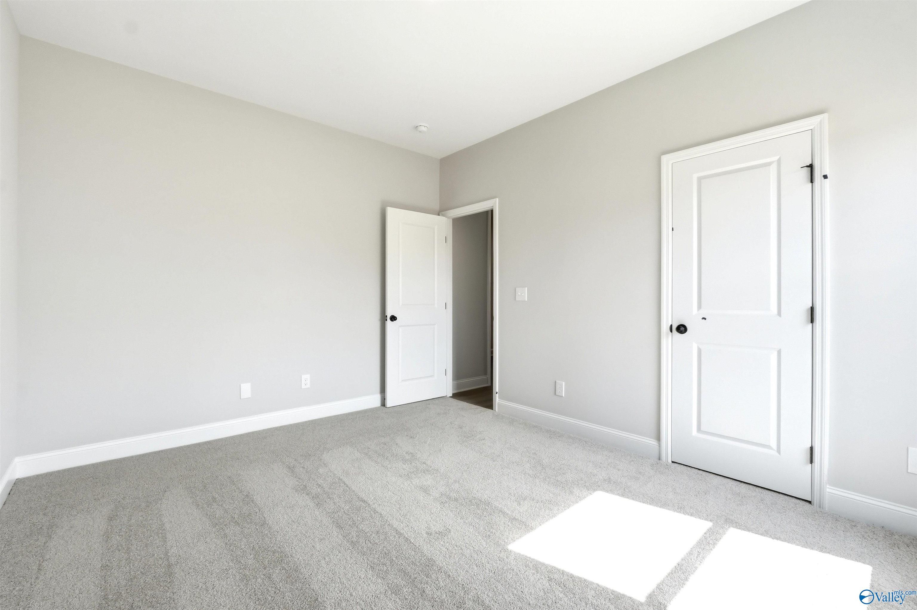 Spacious bedroom with neutral paint and carpet in The Daphne F floor plan at Berry Cove, New Market, Alabama.