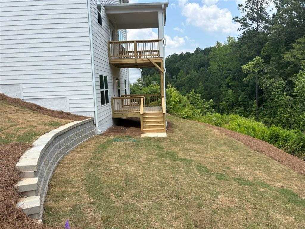 Two-story white home with wooden deck stairs and retaining wall overlooking wooded hillside in Riverwood, Dallas, Georgia