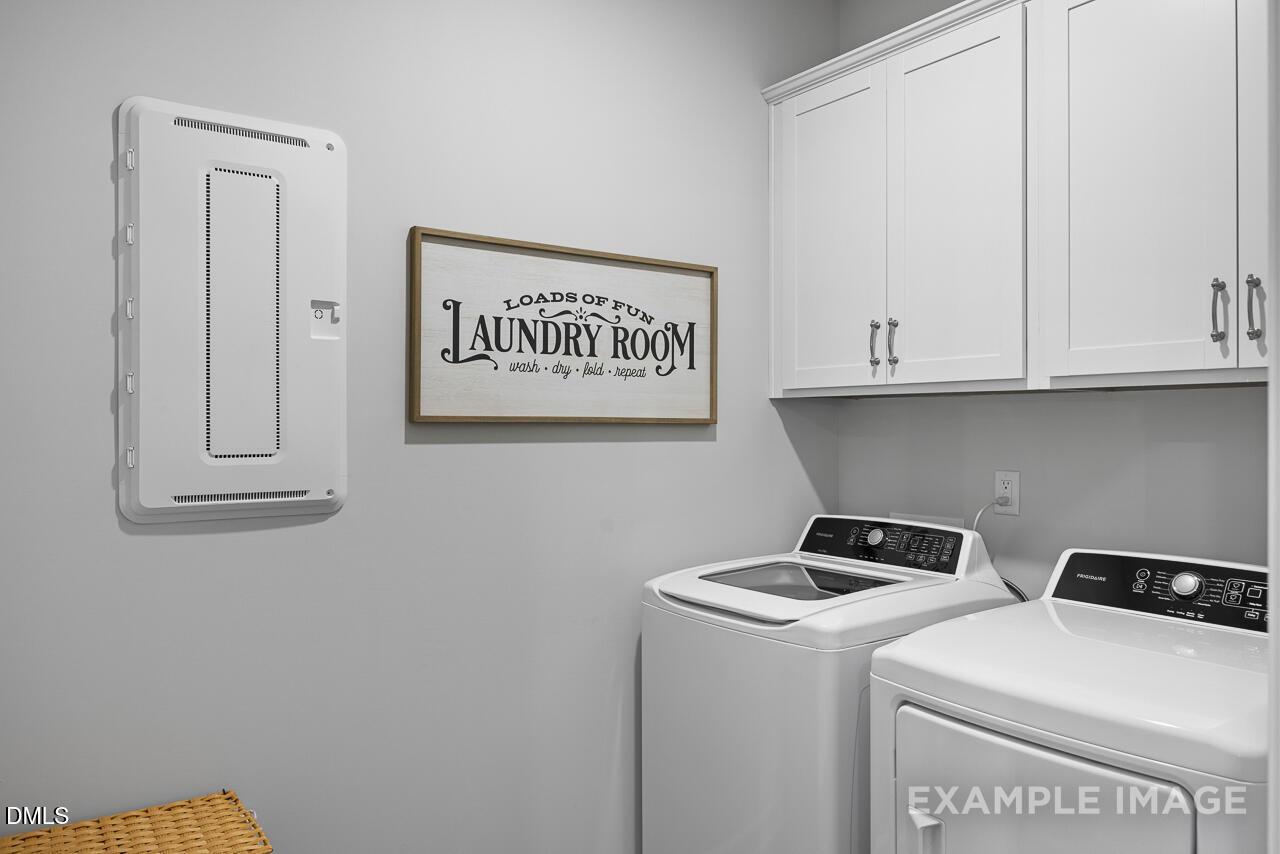 Functional laundry room with white washer, dryer, cabinets, and rustic sign in Davidson Homes The Magnolia B, Angier, NC