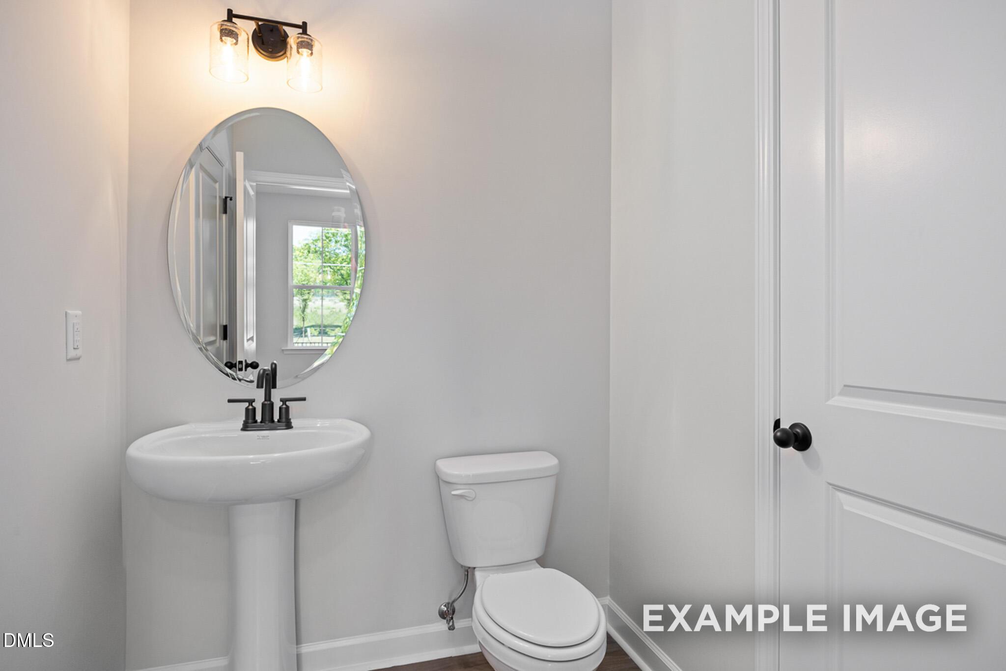 Modern powder room with pedestal sink, oval mirror, and contemporary lighting in The Mitchell home at Camden Park, NC.