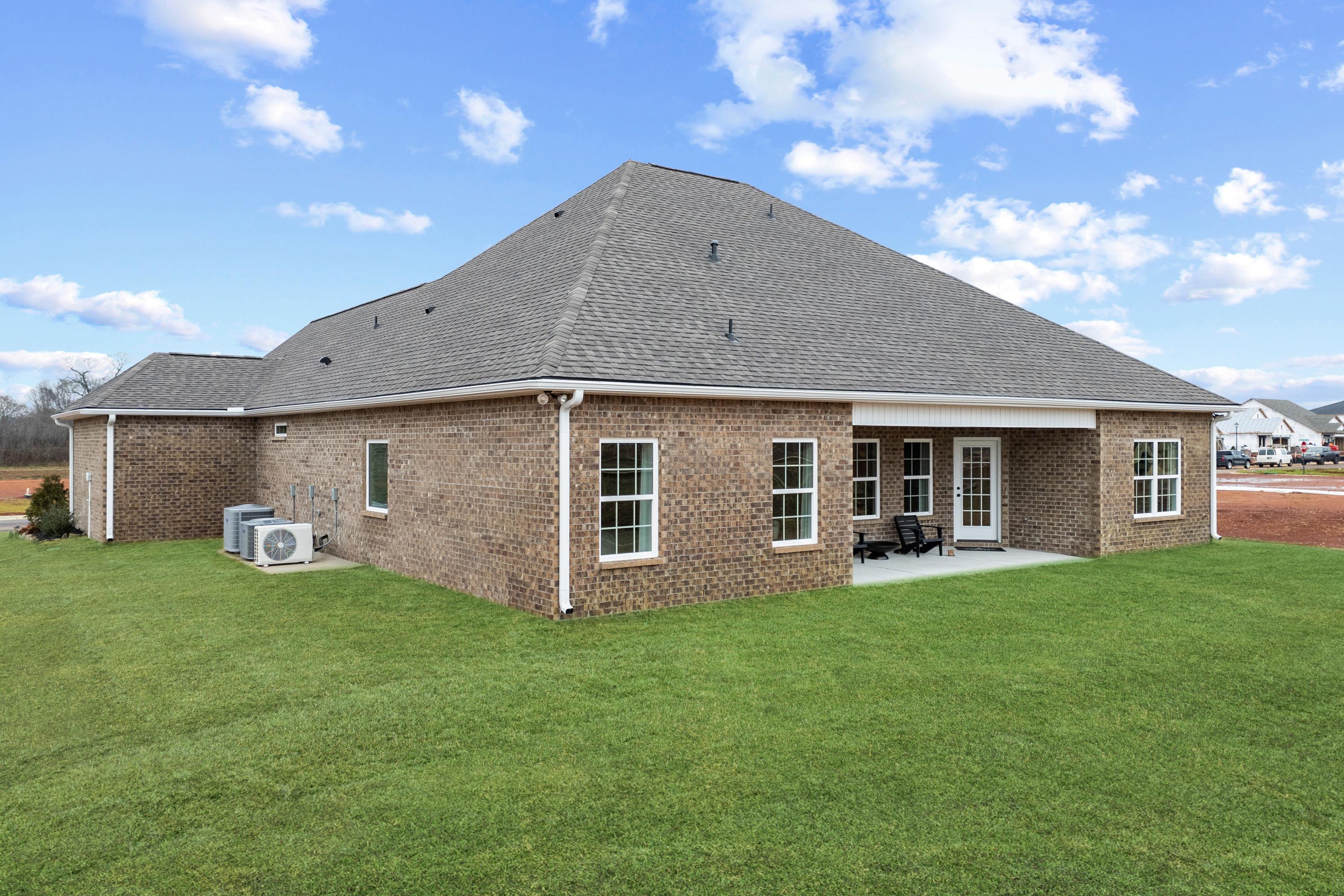 Brick home side exterior with covered patio, French doors, and green lawn at Kendall Farms in Toney, Alabama
