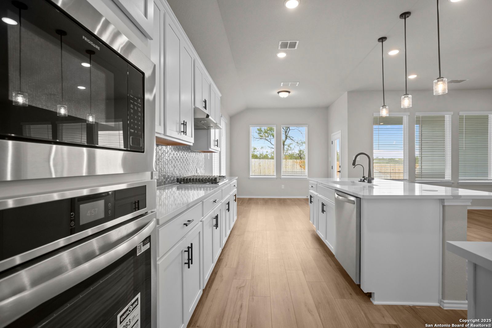 Modern white kitchen with stainless double ovens, island sink, and backyard view via large windows in Davidson Homes The Sequoia A, Converse, Texas