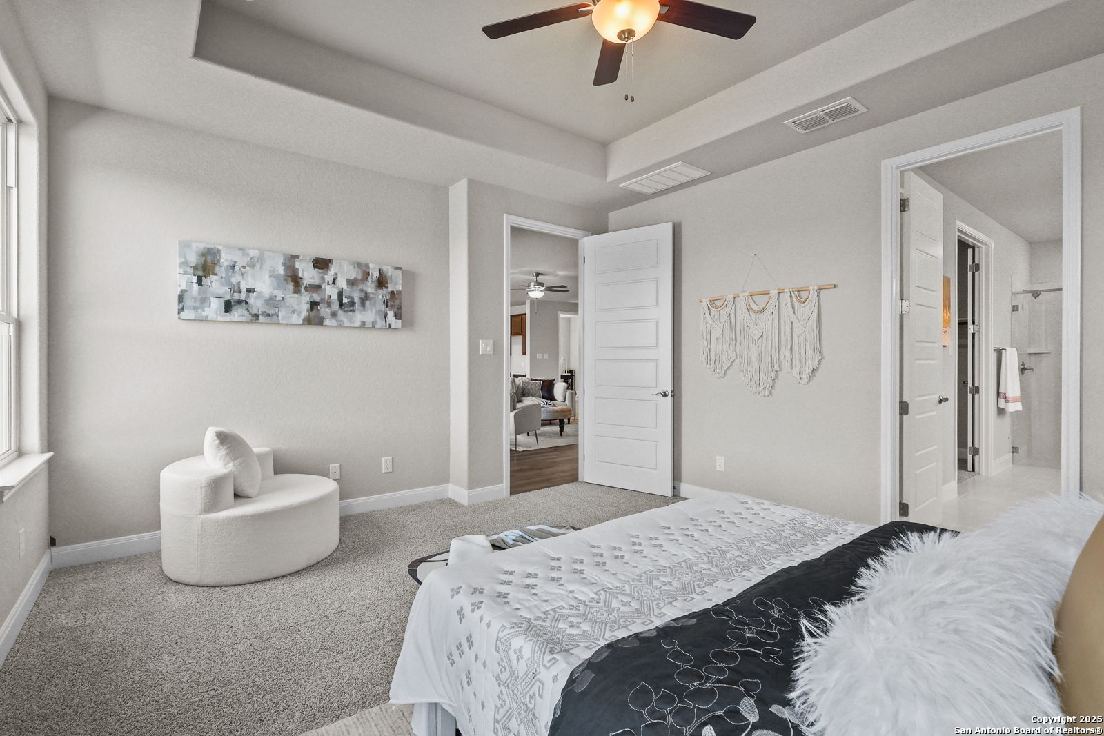 Elegant master bedroom with plush king bed, ceiling fan, abstract art, and en-suite bath in Davidson Homes The Jennings G, Castroville, Texas