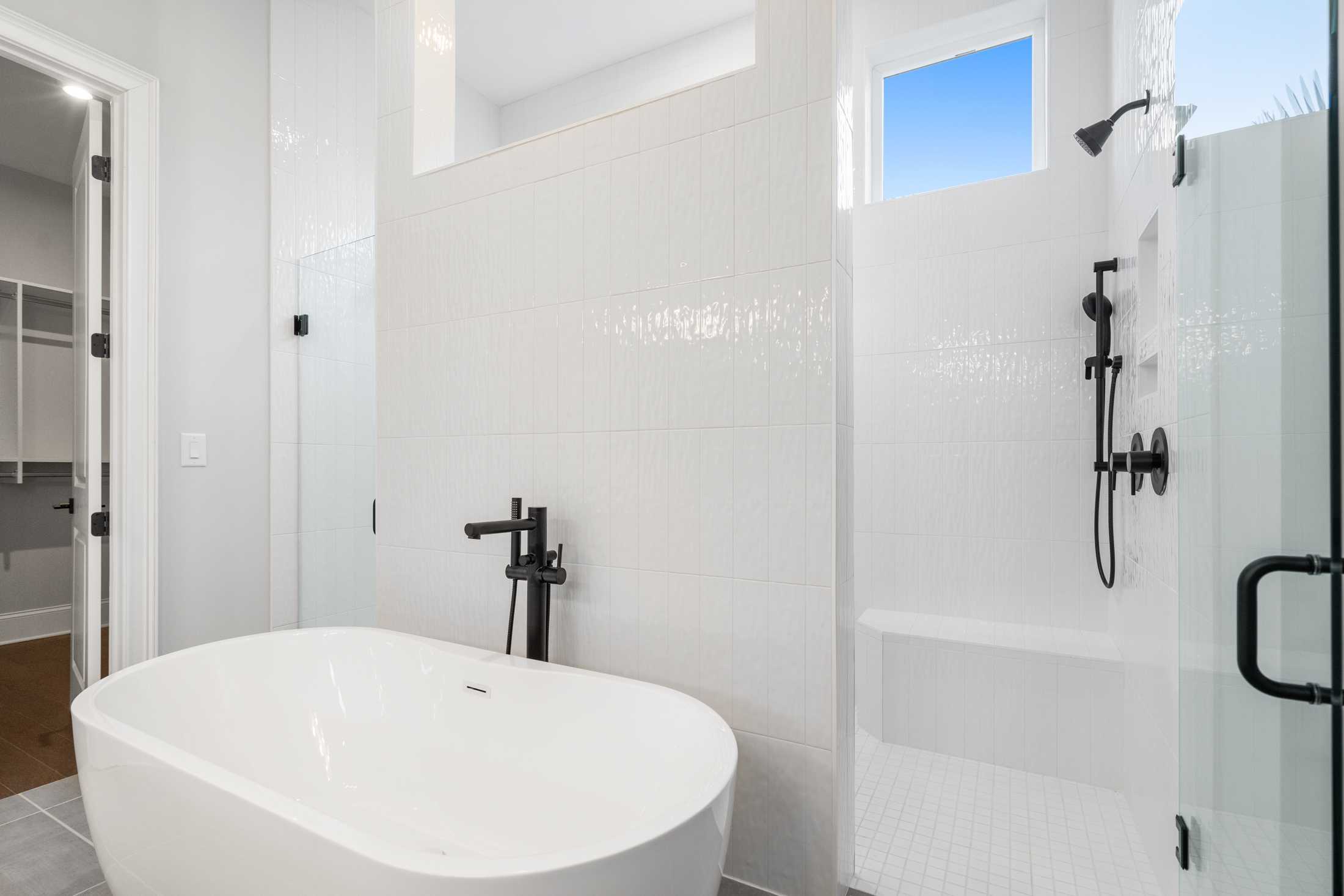 Luxurious master bathroom in The Seaside featuring freestanding soaking tub, glass walk-in shower, white subway tiles, black fixtures