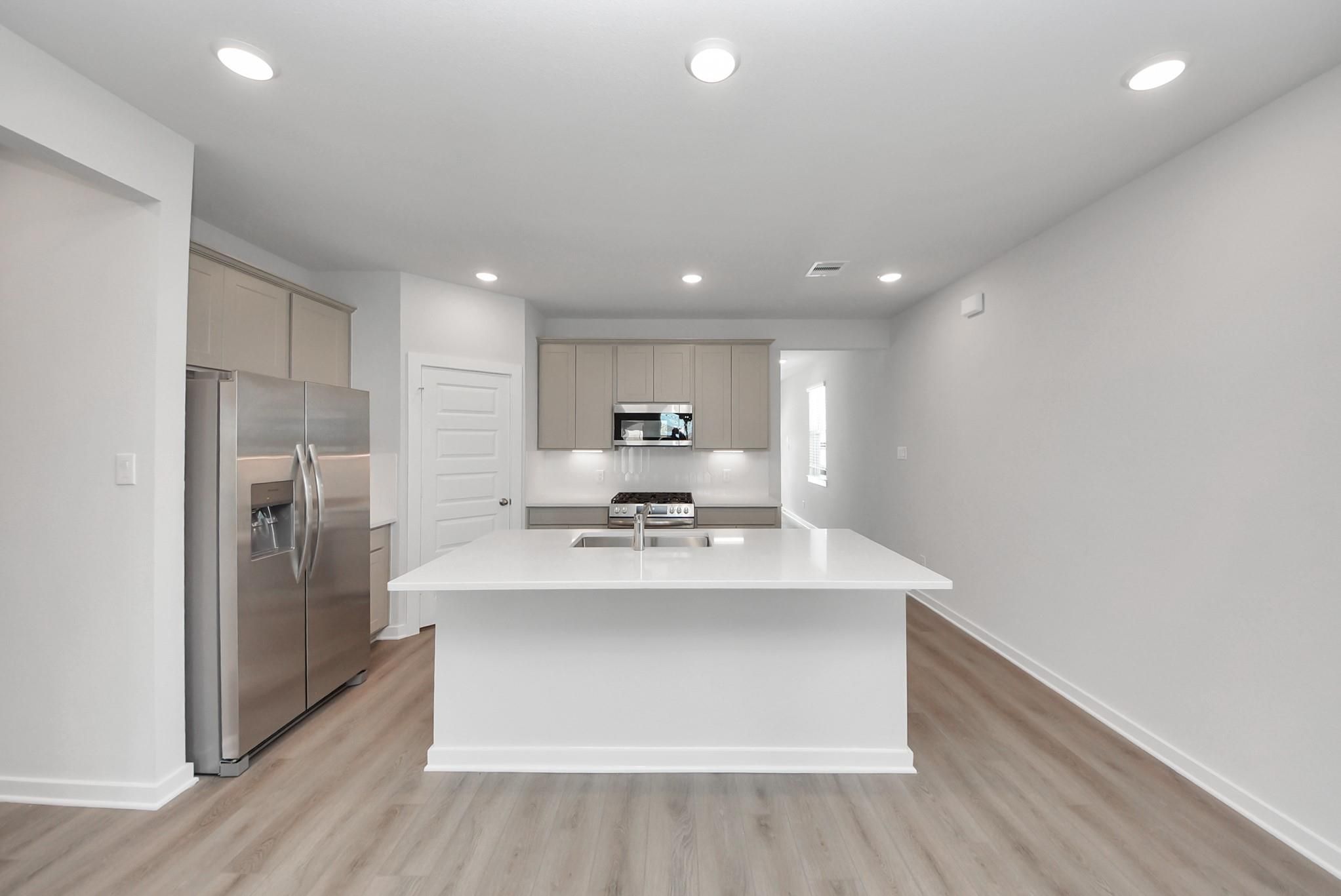 Bright kitchen with white island, quartz countertops, stainless appliances, and wood-look flooring in Davidson Homes San Marcos E plan