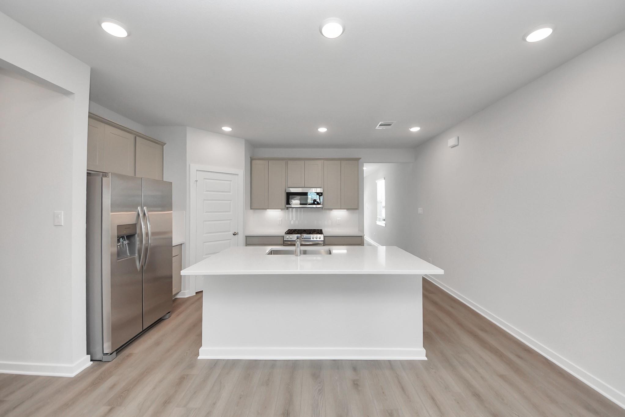 Bright kitchen with white island, quartz countertops, stainless appliances, and wood-look flooring in Davidson Homes San Marcos E plan