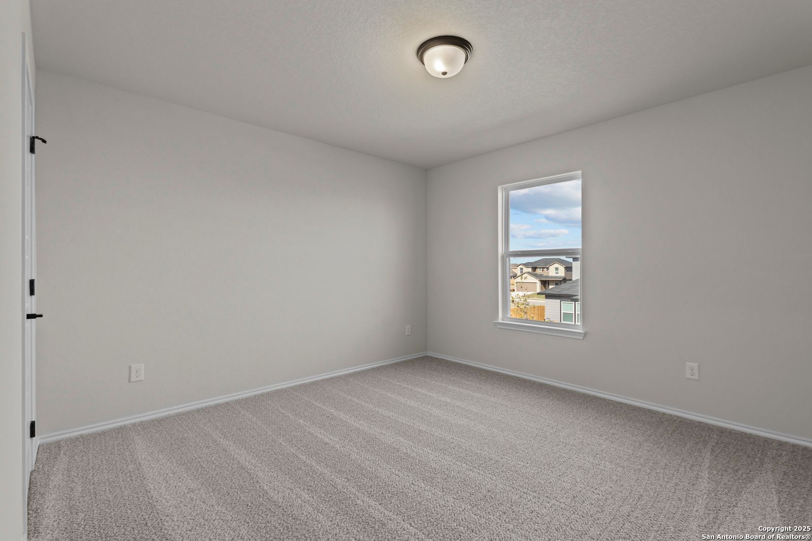Bright secondary bedroom with neutral gray walls, plush carpet, and window overlooking Hannah Heights in Seguin, Texas