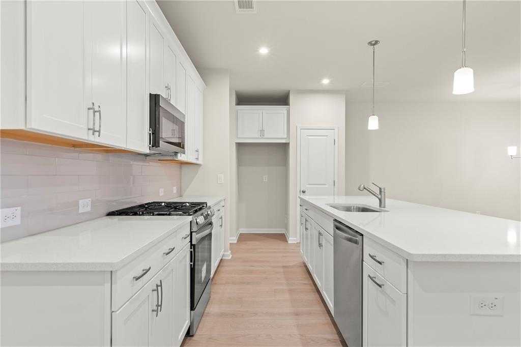 Modern white kitchen with stainless appliances, subway tile backsplash, island, and hardwood floors in Davidson Homes The Cary A, Kennesaw, GA