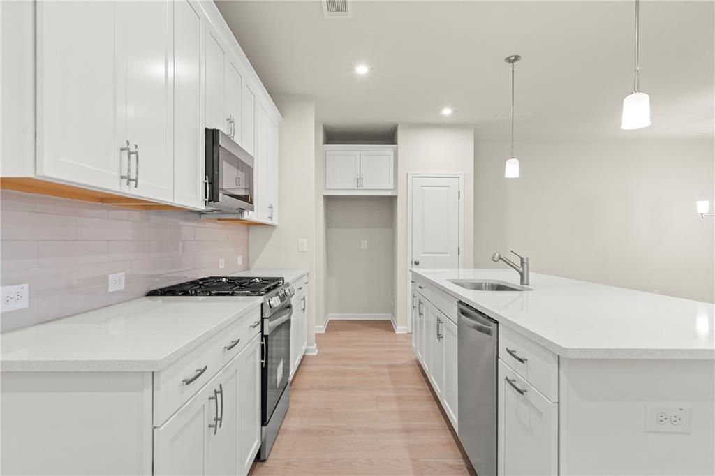 Modern white kitchen with stainless steel appliances, subway tile backsplash, and large island in Davidson Homes The Cary A, Kennesaw, GA