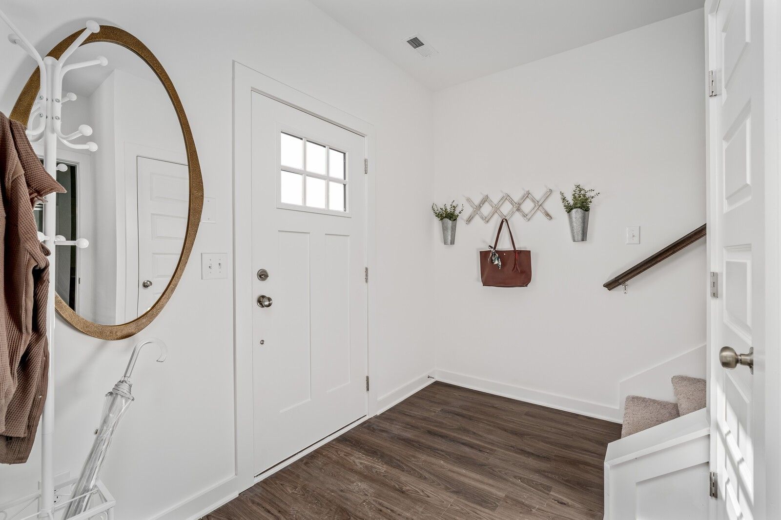 Bright entryway with gold-framed round mirror, coat rack, hanging purse, wall decor, and staircase in Davidson Homes The Cumberland A, Gallatin, TN