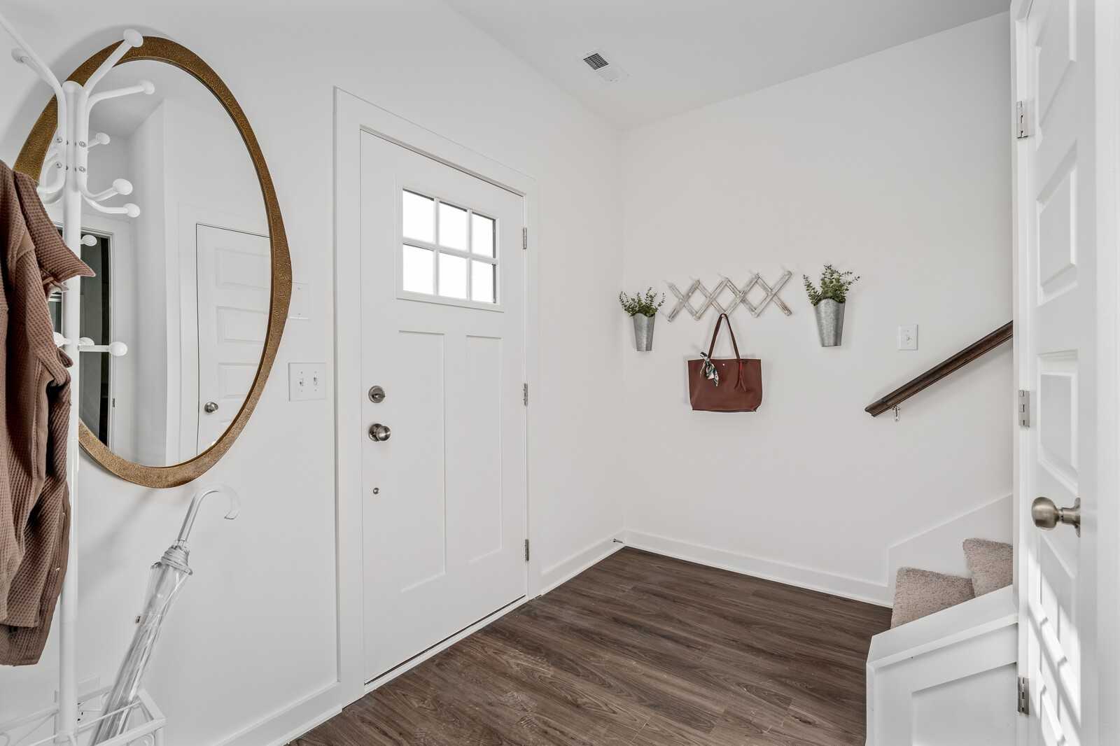 Bright entryway with gold-framed round mirror, coat rack, hanging purse, wall decor, and staircase in Davidson Homes The Cumberland A, Gallatin, TN