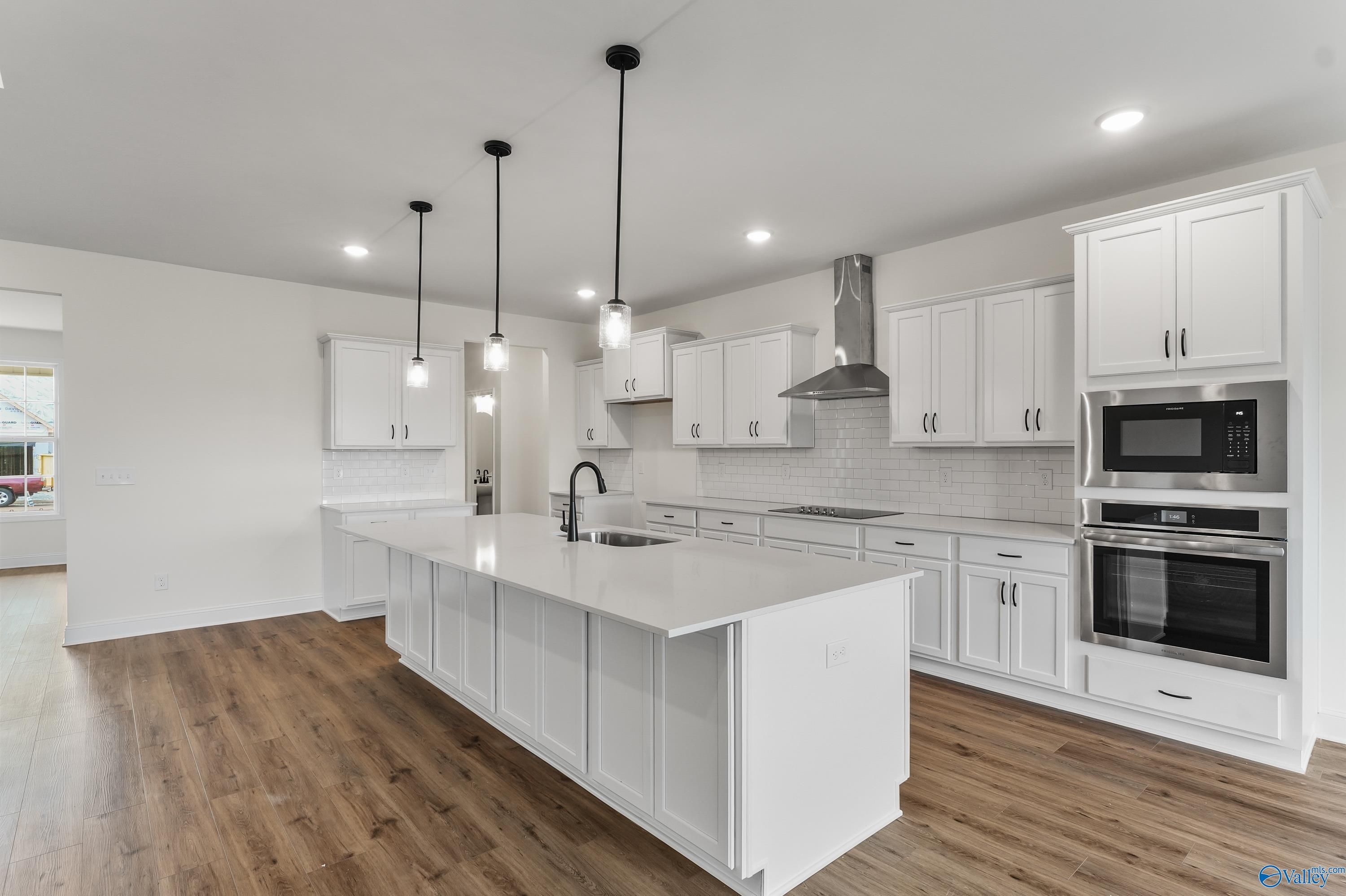 Modern white kitchen island with sink, stainless steel ovens and range hood in The Finleigh plan by Davidson Homes, Harvest, Alabama