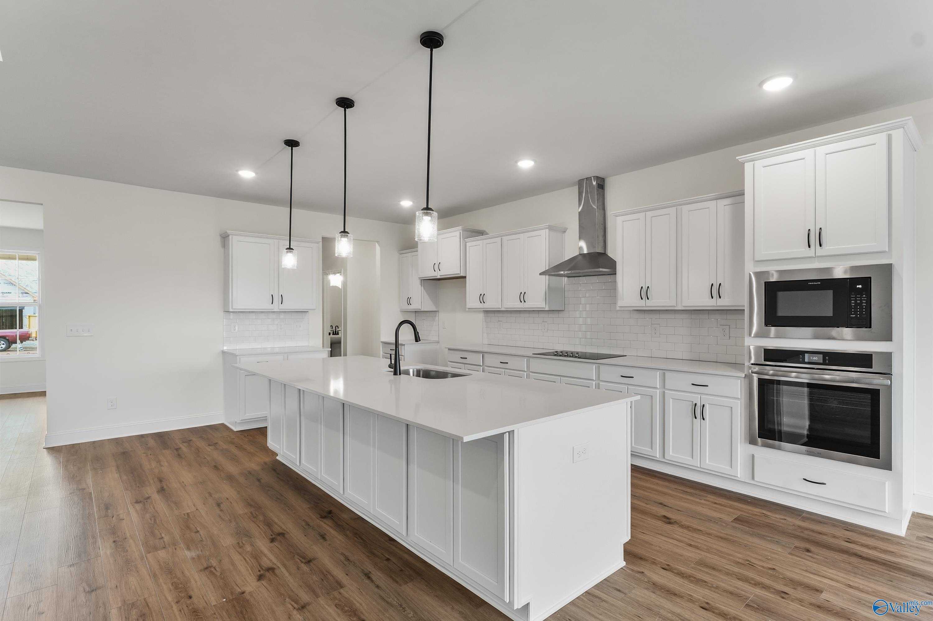 Modern white kitchen island with sink, stainless steel ovens and range hood in The Finleigh plan by Davidson Homes, Harvest, Alabama