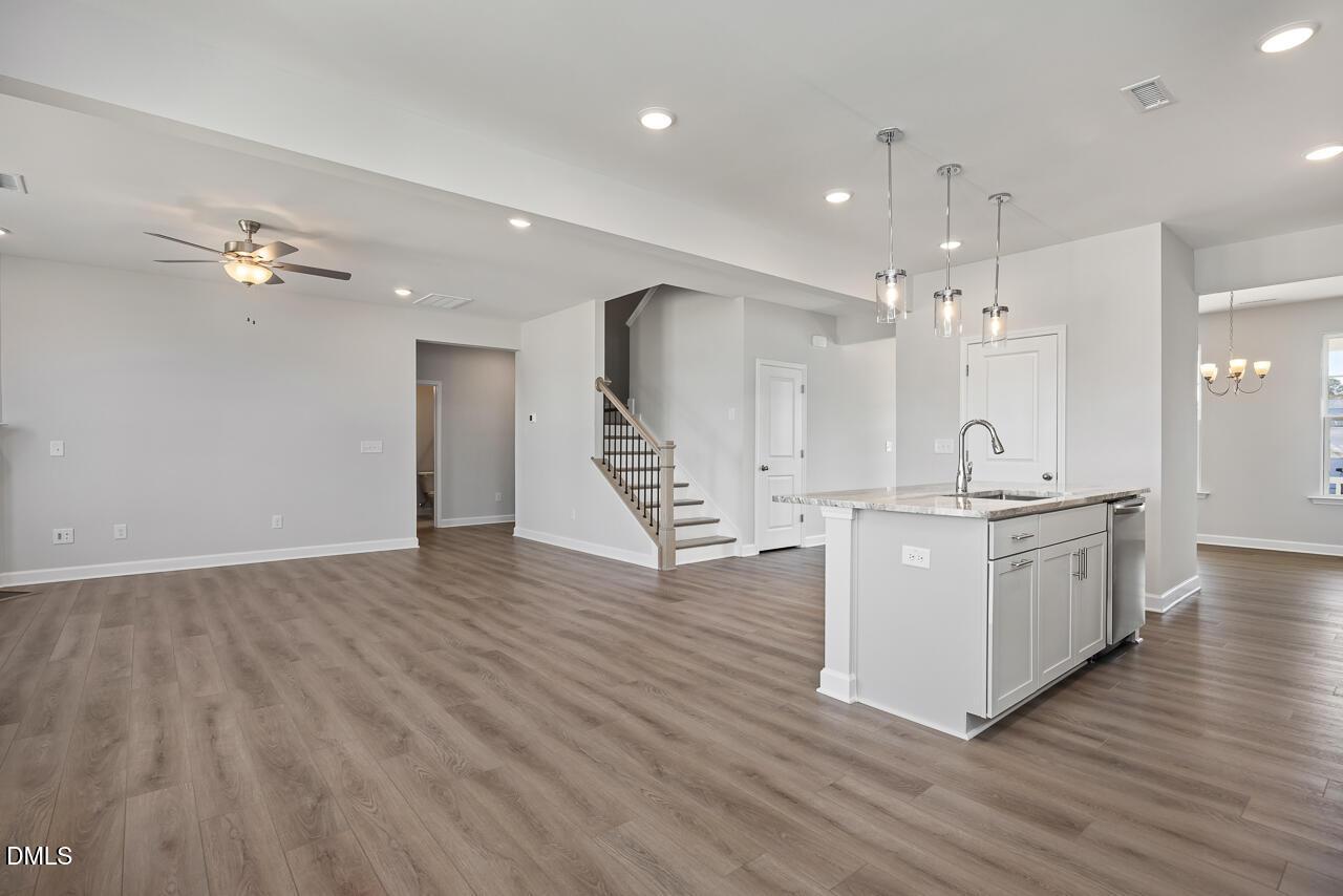 Open-concept living and kitchen with white island, pendant lights, hardwood floors, and staircase in The Willow G home, Angier, NC