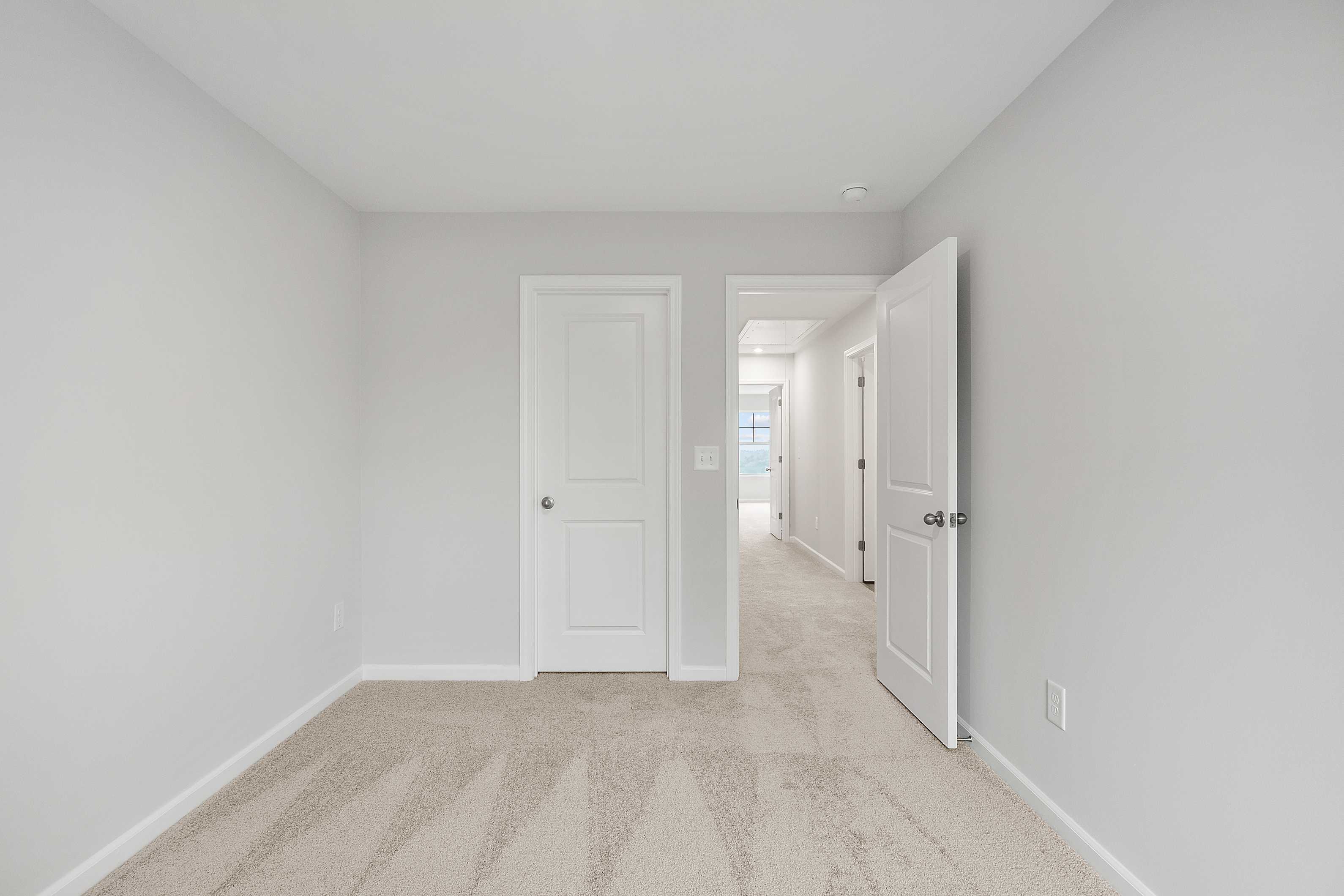 Spacious secondary bedroom in The Durant A with light gray walls, white doors, beige carpet, and hallway access