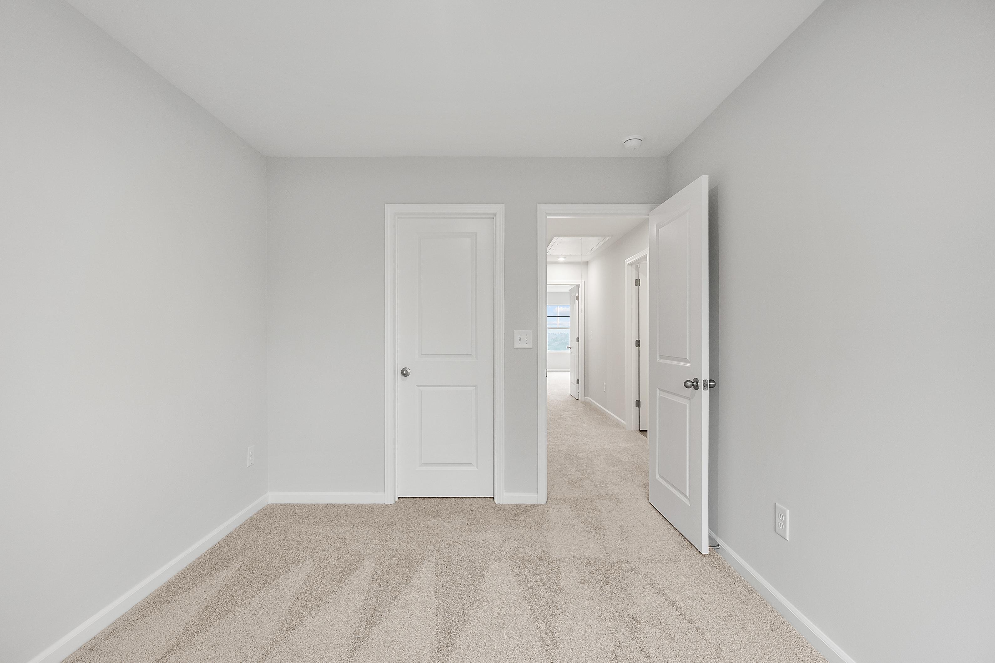 Spacious secondary bedroom in The Durant A with light gray walls, white doors, beige carpet, and hallway access