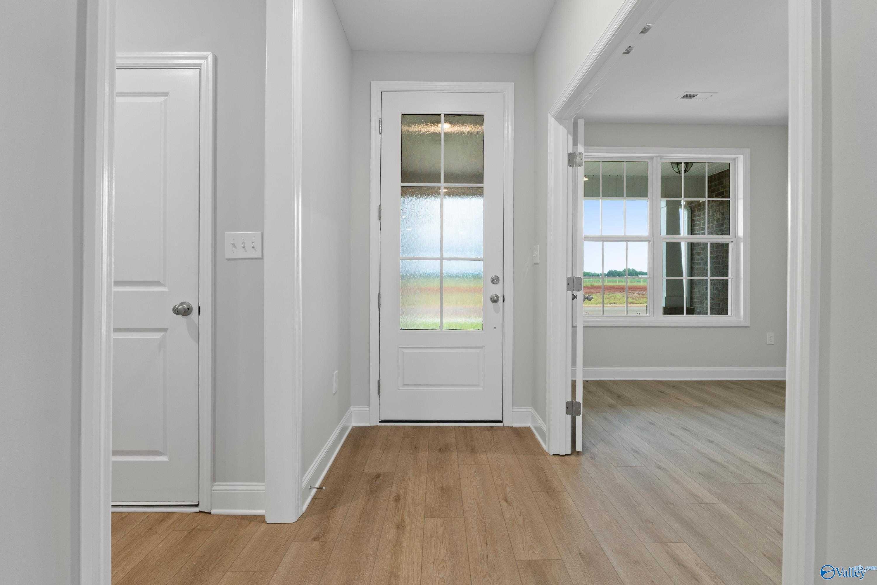Bright entryway with hardwood floors and white glass-paneled door overlooking green lawn in Davidson Homes The Rockford B, Toney AL
